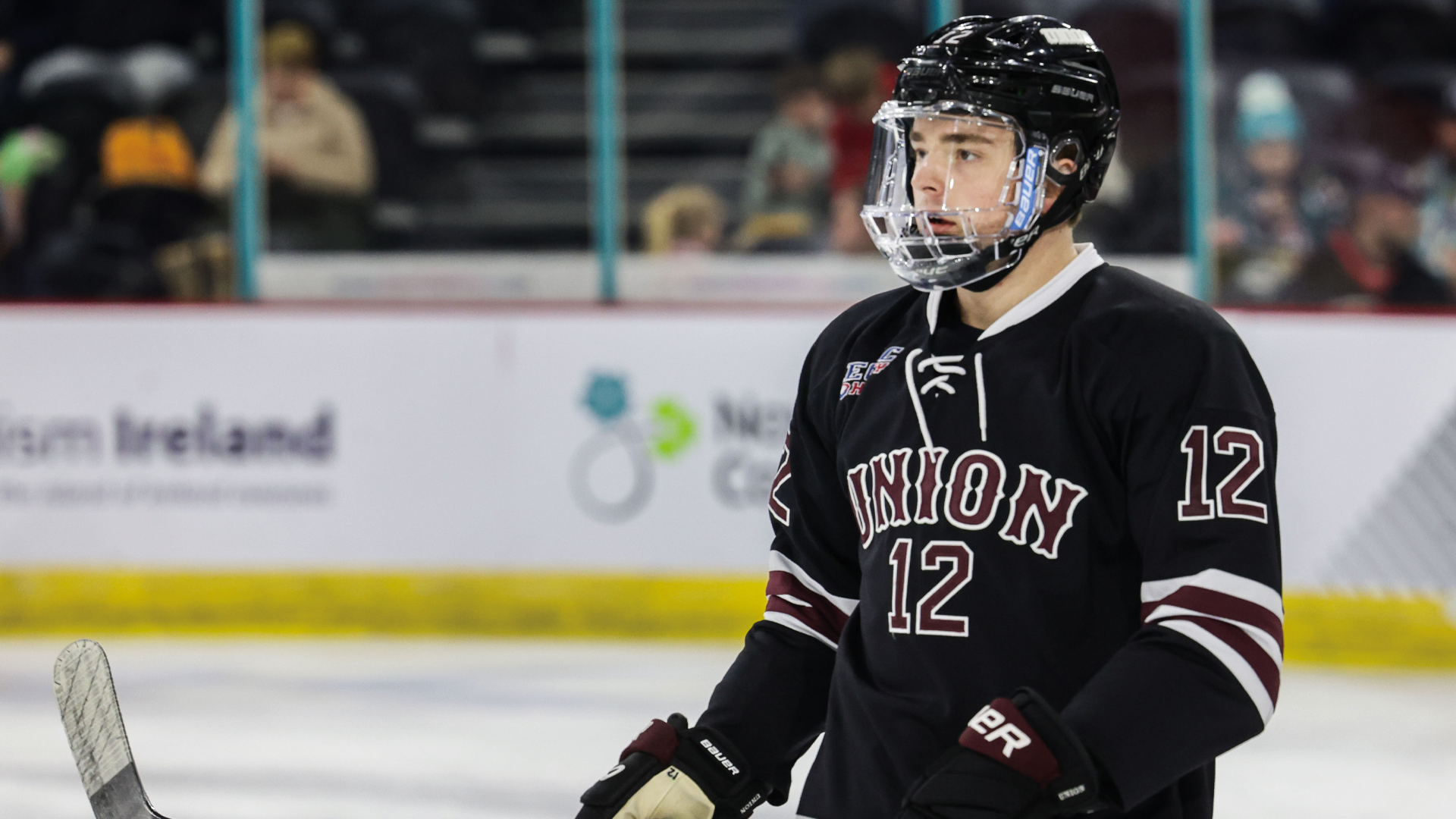 men's hockey player wearing a black jersey and black helmet, photographed from the waist up looking to his right