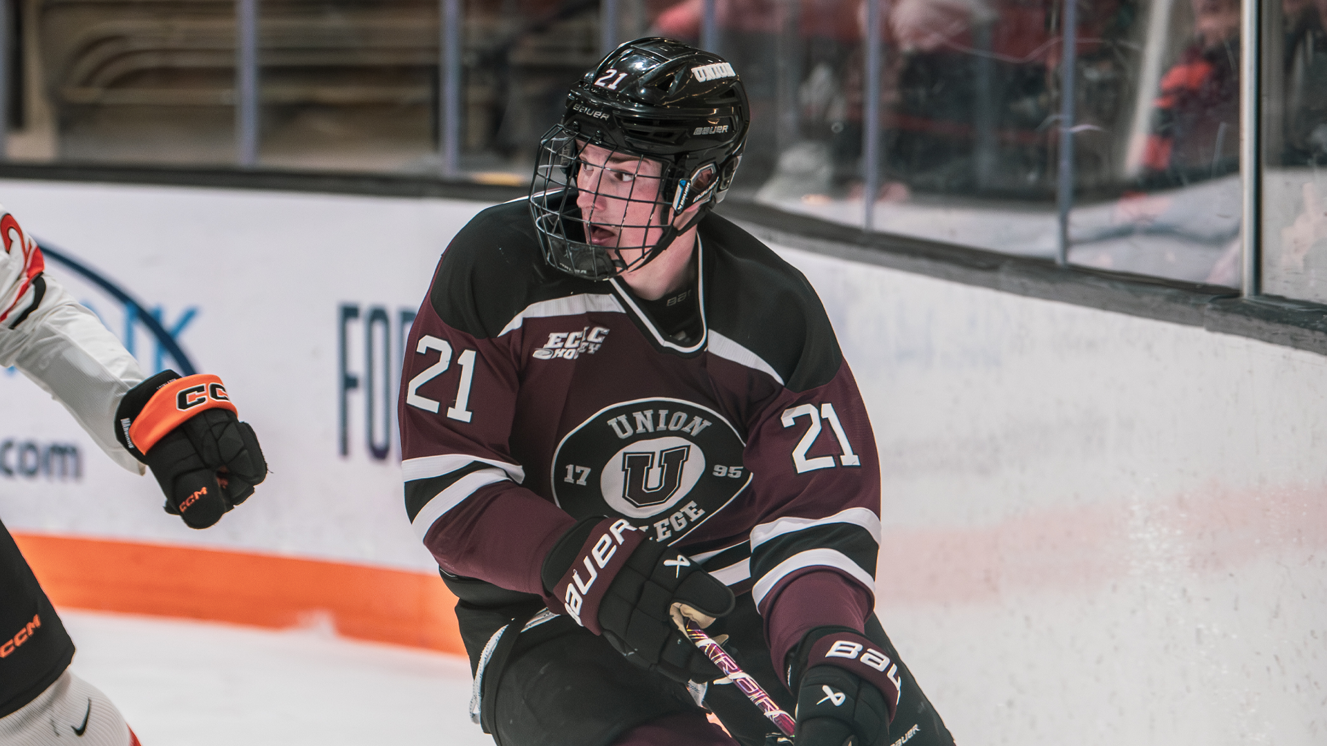 a men's hockey player looking to his right while skating near the boards