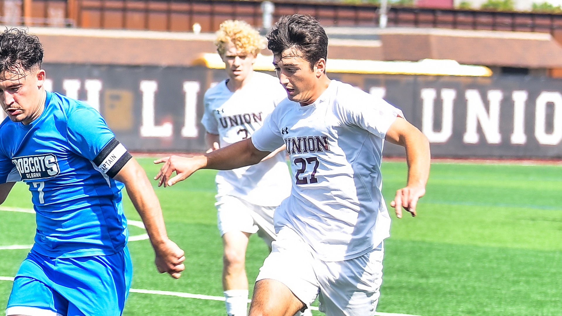 A men's soccer player chases an opponent for the ball.