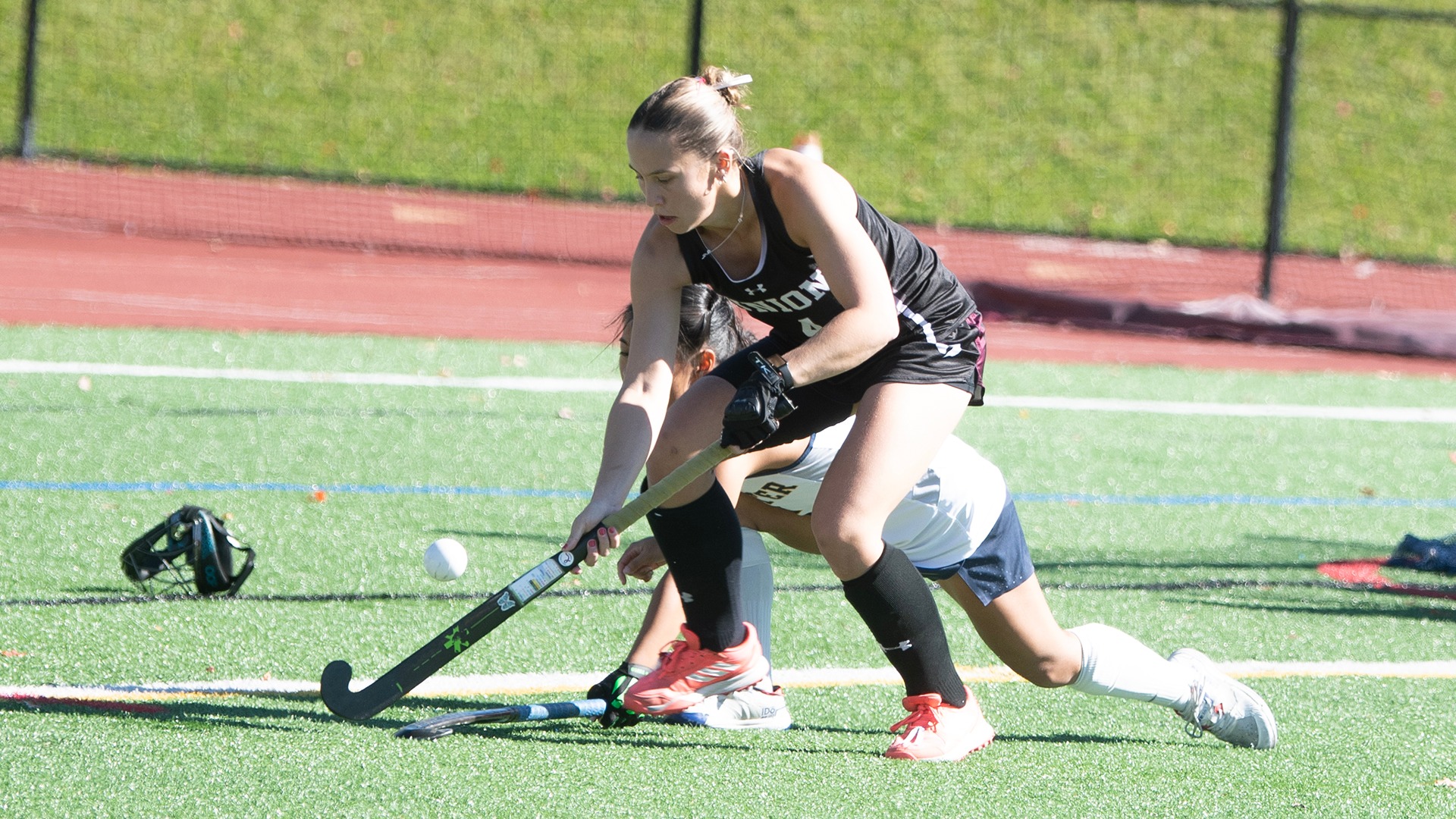 A field hockey player stickhandles the ball with a defender behind her.
