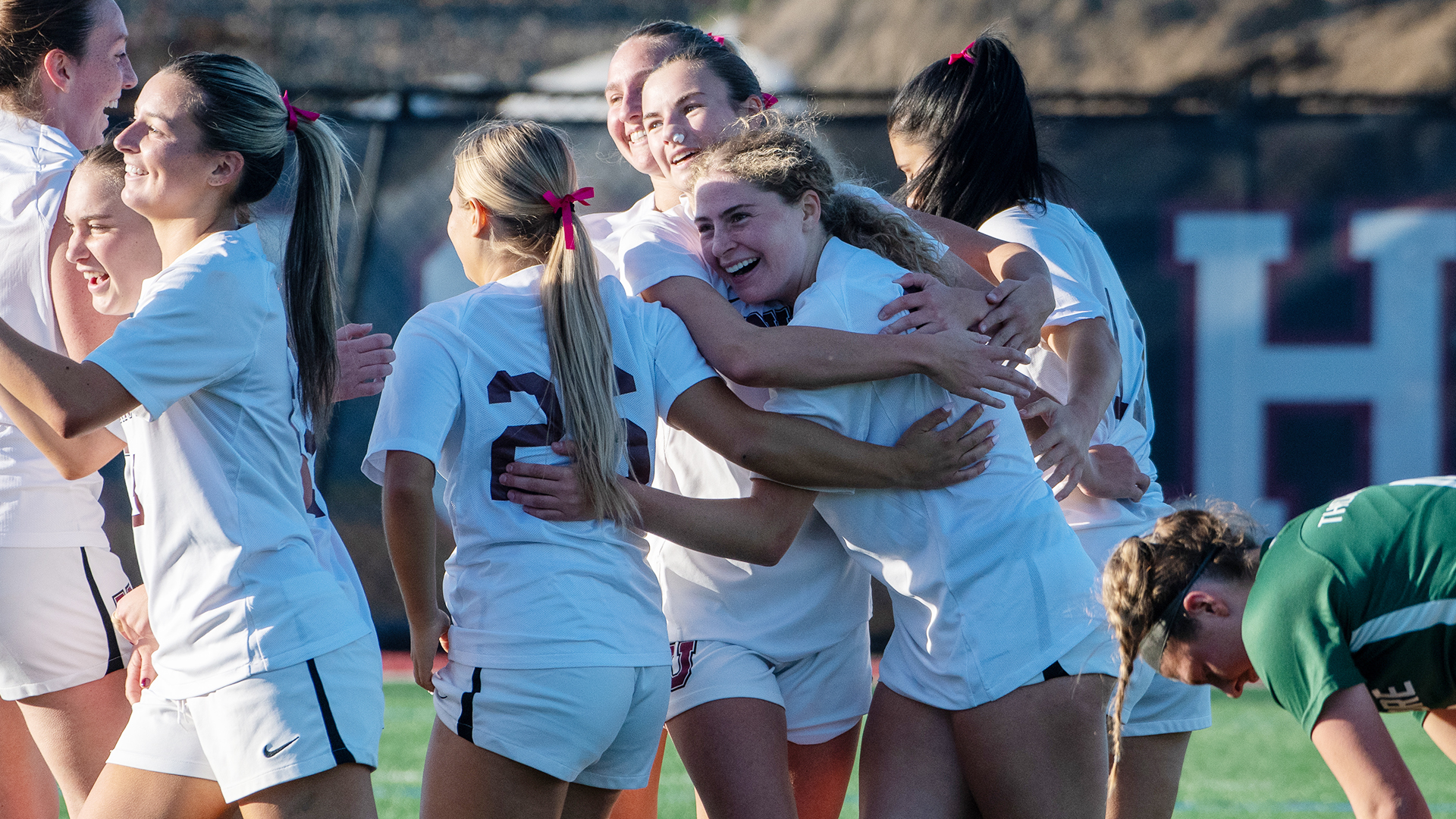 A group of women's soccer players smiling and hugging after a goal.