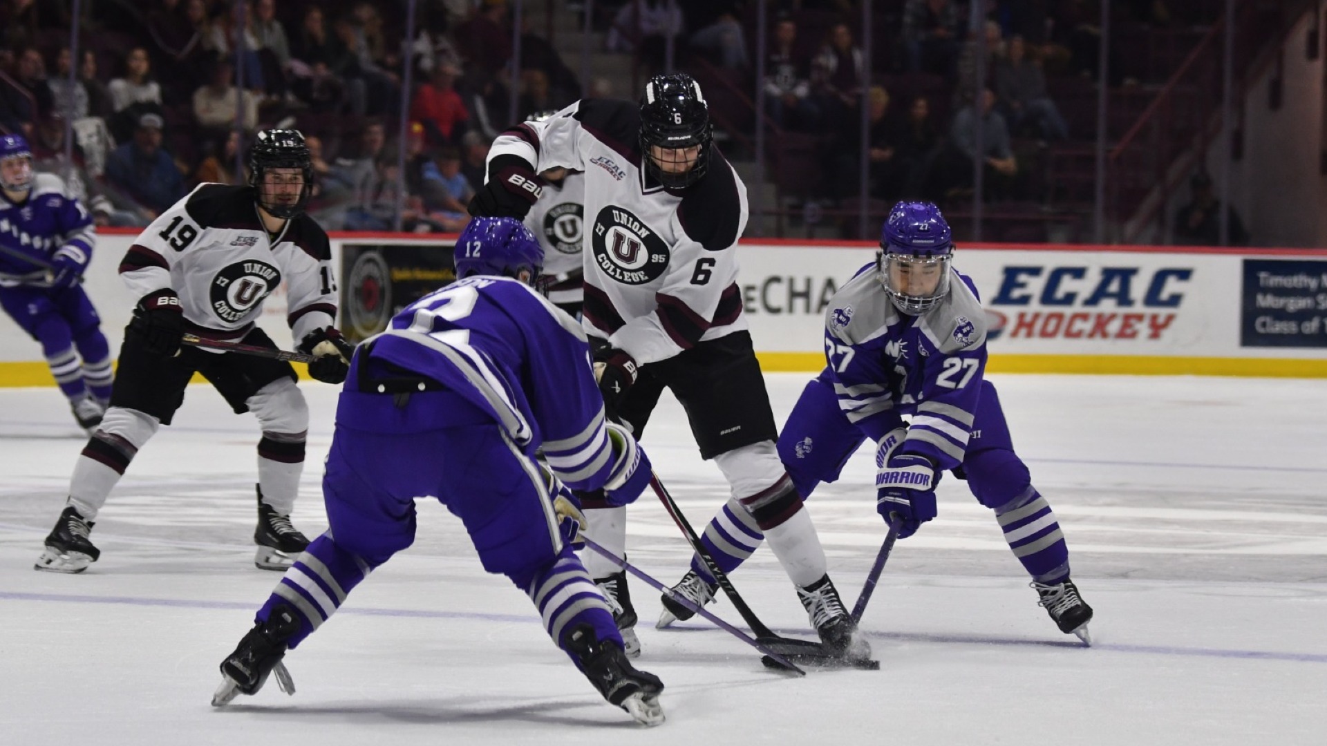 a men's hockey player skating with two opponents in front and behind him