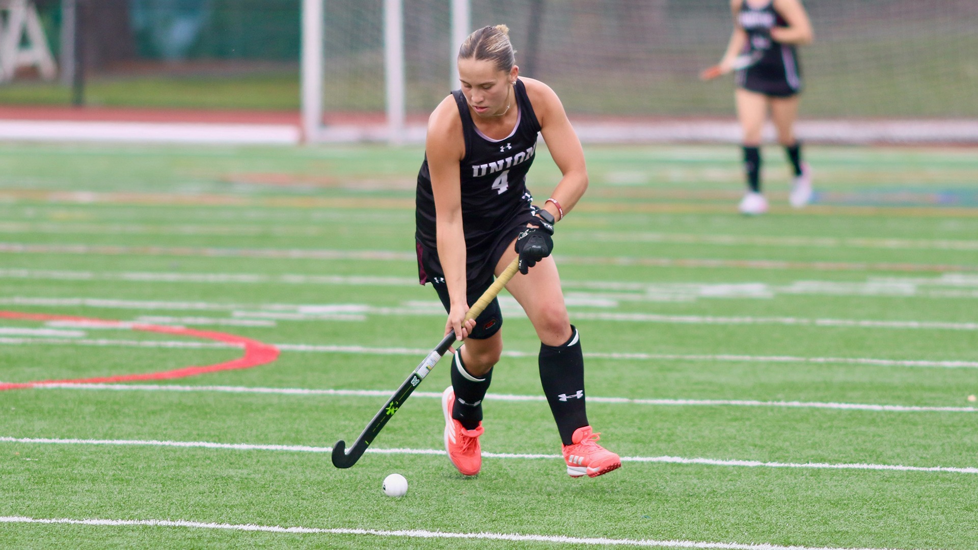A field hockey player looks down as she stickhandles down the field.