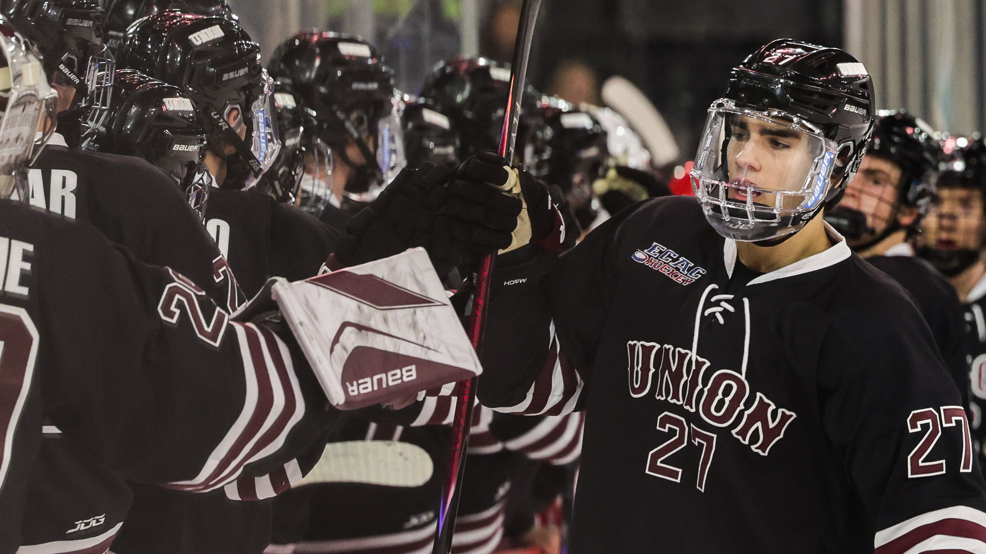 a men's hockey player skating past his bench after a goal to celebrate with his teammates