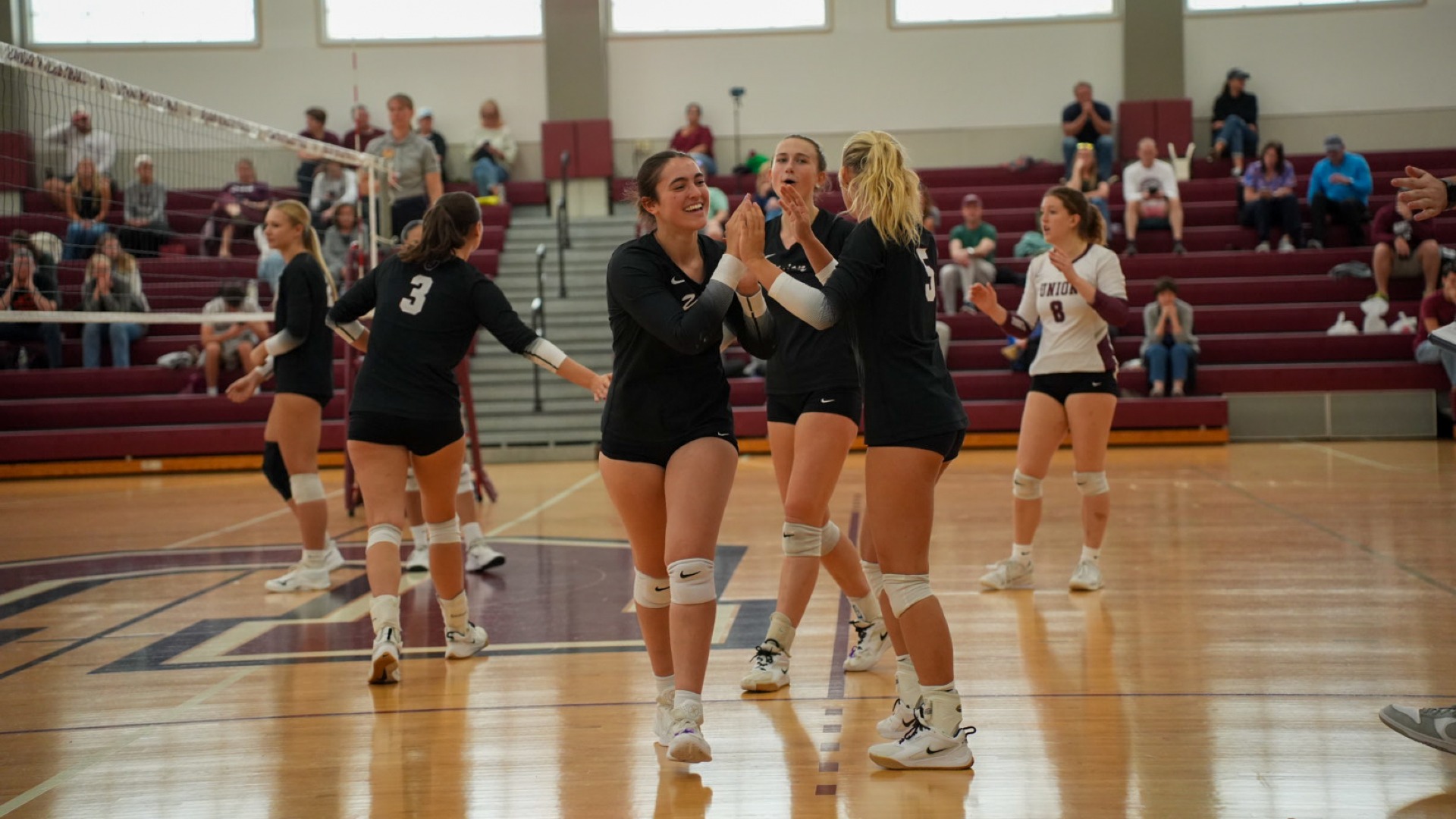 women's volleyball players high-fiving and smiling while making a substitution