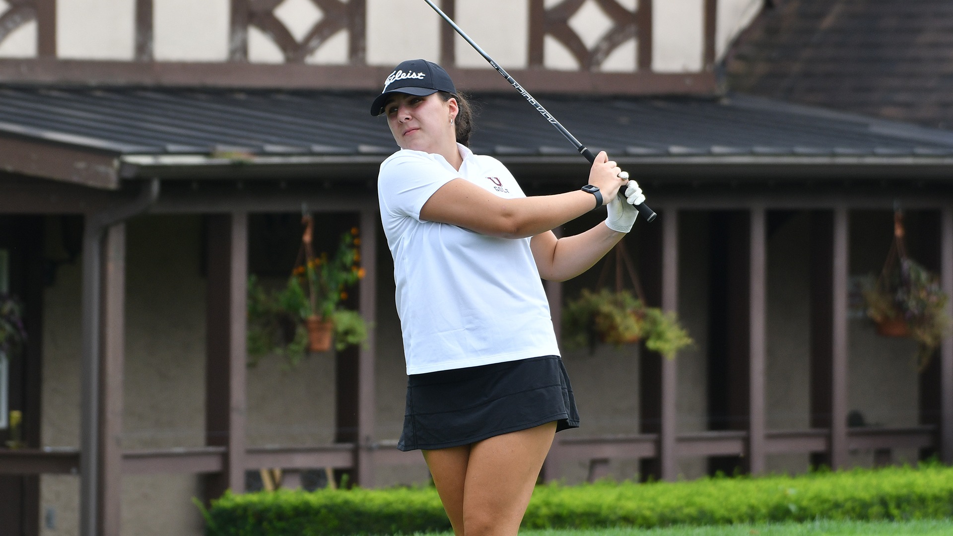 A women's golfer watches her drive after a follow through.