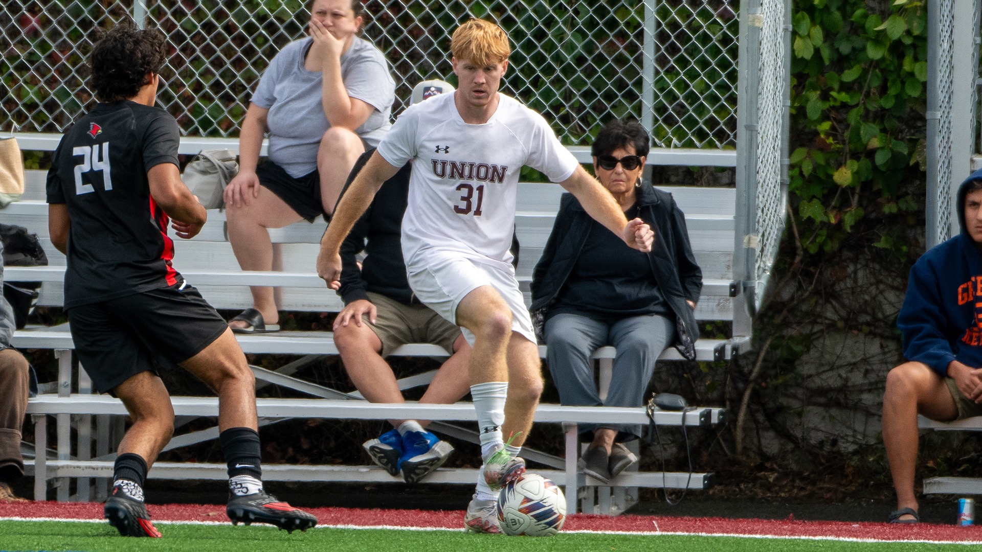 A men's soccer player with the ball at his feet and a defender running toward him.