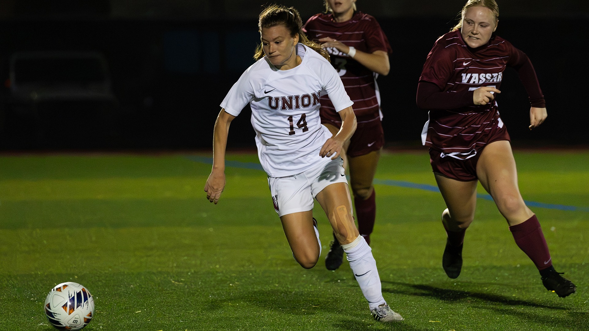 A defender dribbles away from two defenders behind her.