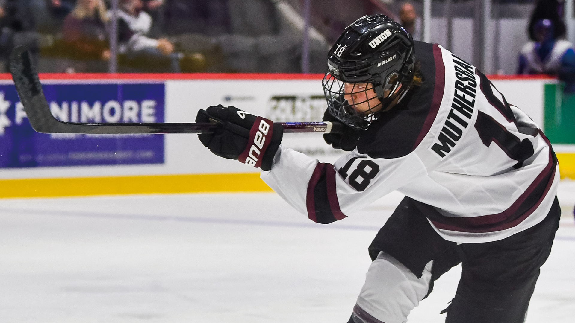 a men's hockey player with his back to the camera as he is midway through the follow through of his slapshot