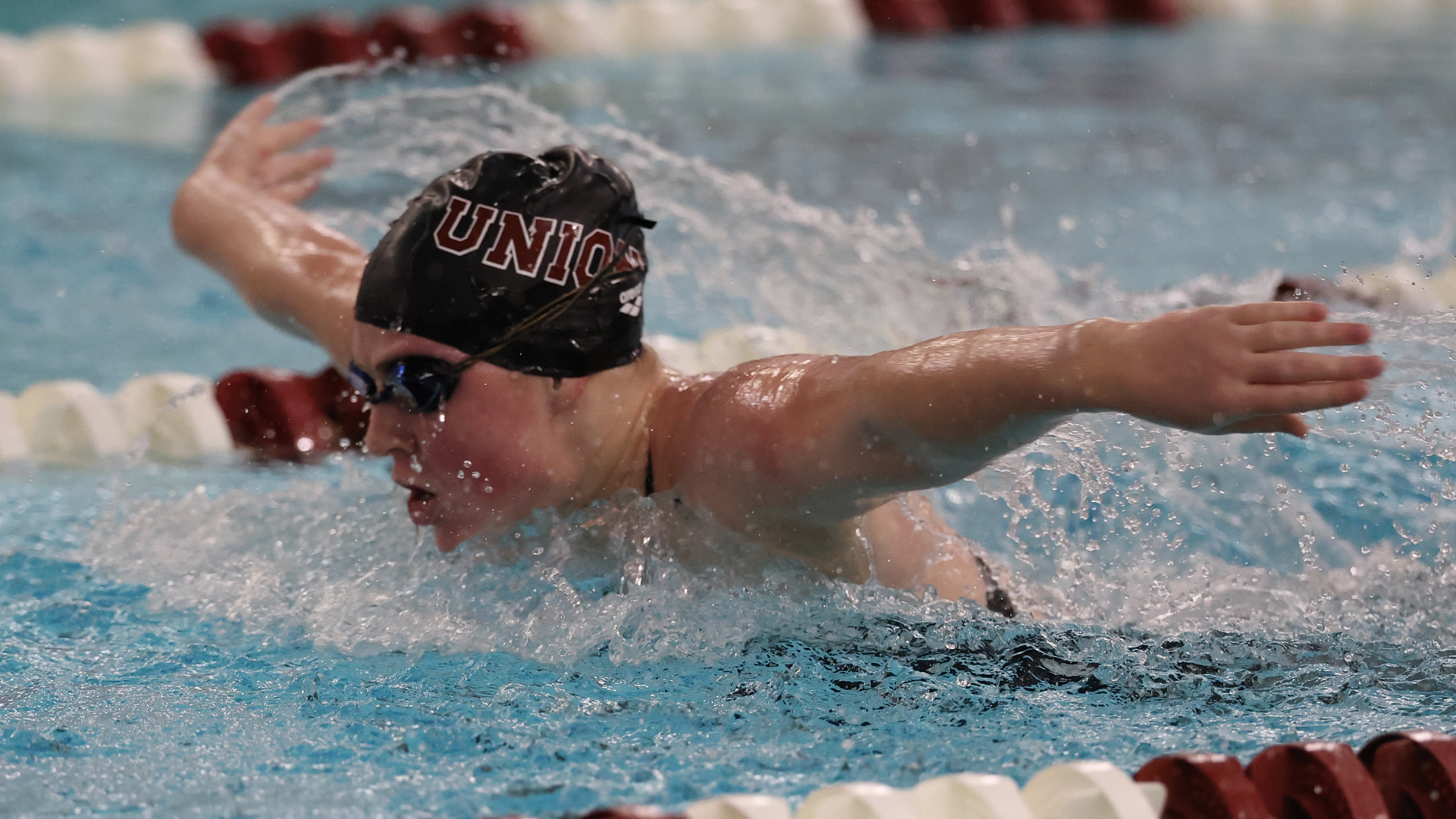 women's swimmer performing the butterfly, wearing a black swim cap that reads 