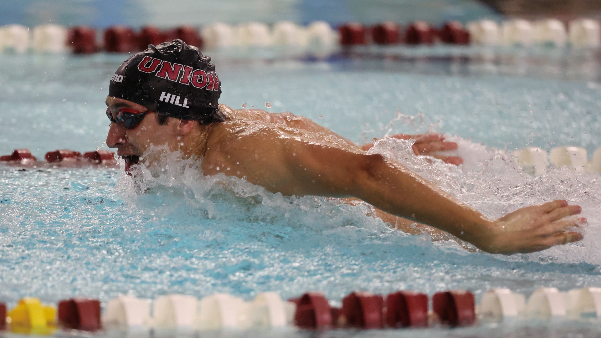men's swimmer performing the butterfly, wearing a black swim cap that reads 