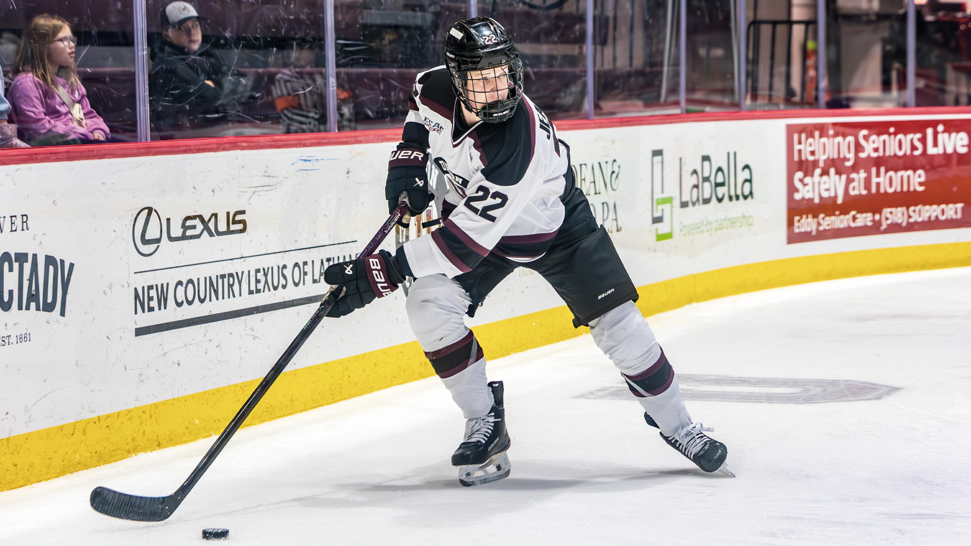 a men's hockey player skating along the boards with the puck on his stick as he looks over his shoulder up at the ice 