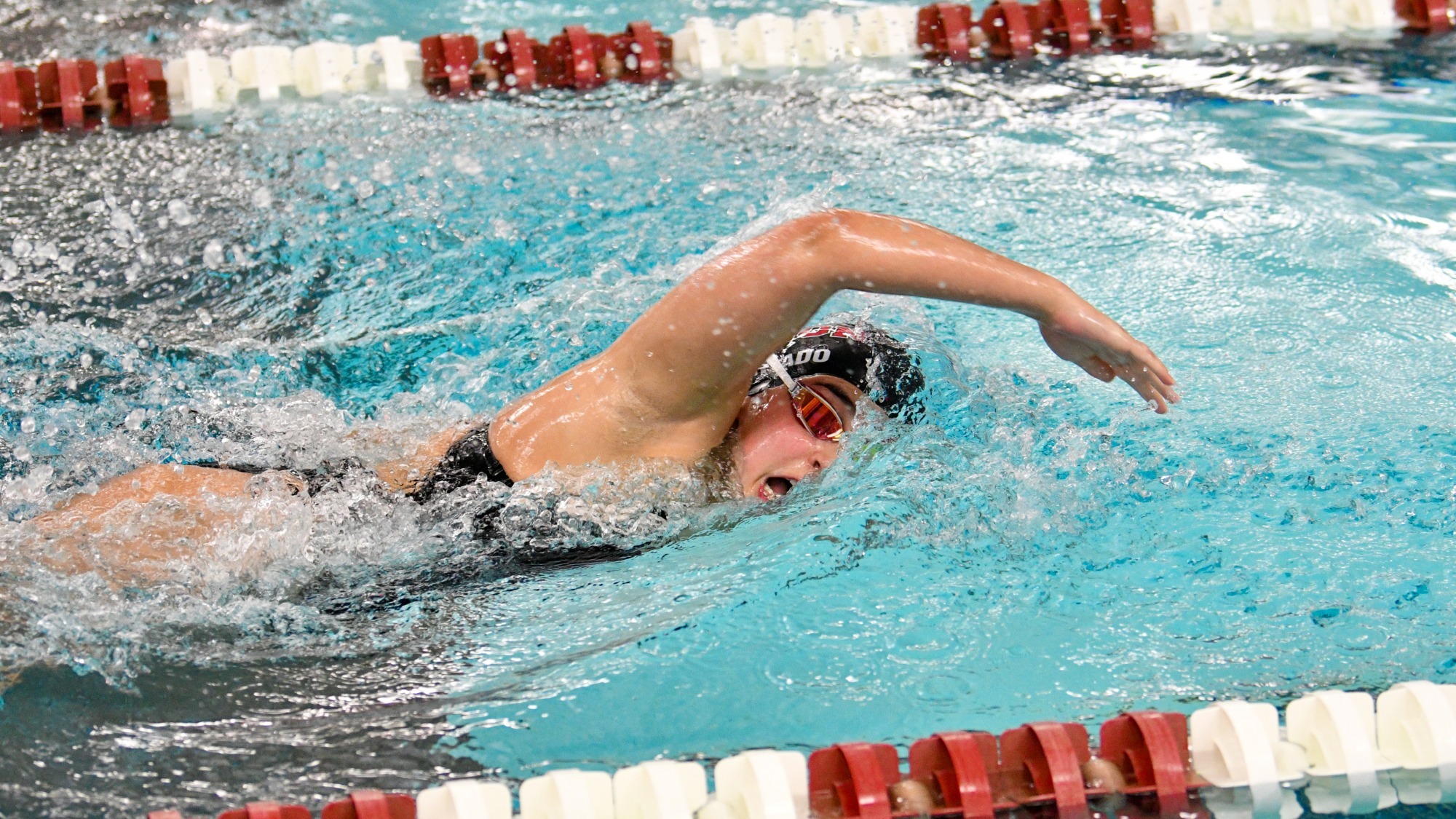 a women's swimmer performing the front crawl, with her face turned to the right to take a breath and her right arm above her head as she is about to enter it into the water
