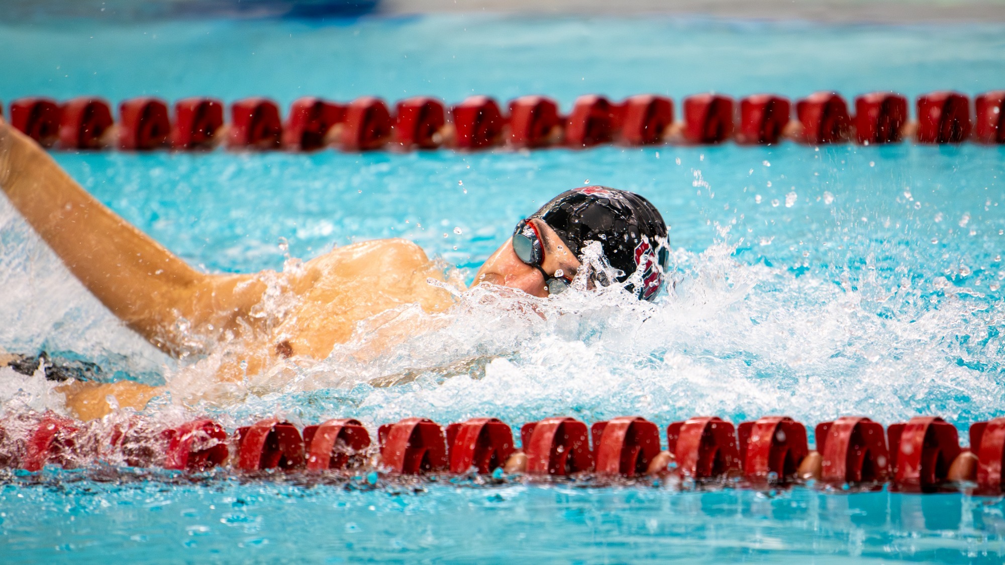 men's swimmer performing the front crawl, swimming from left to right, with his face turned to the right and half out of the water, with his right arm also out and back in the middle of his stroke