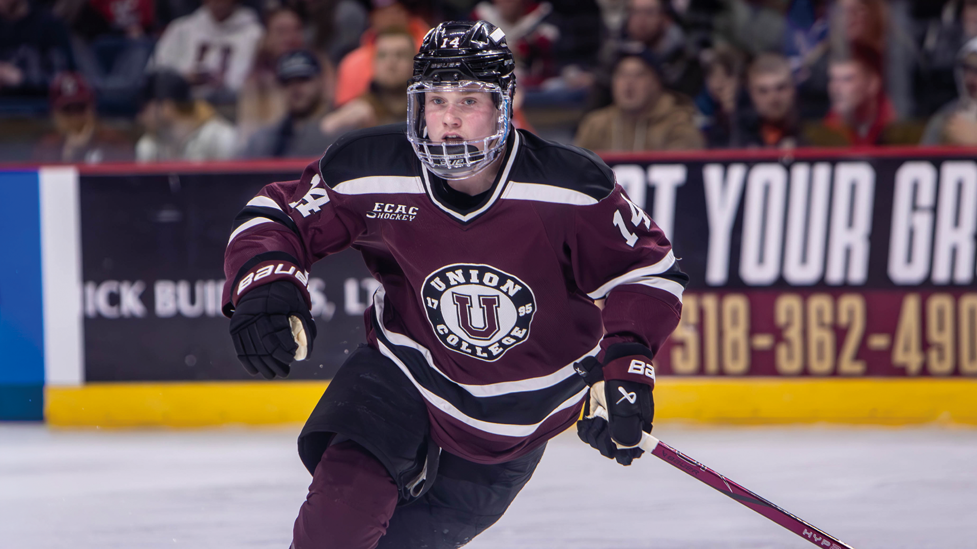 a men's hockey player skating while wearing a garnet jersey
