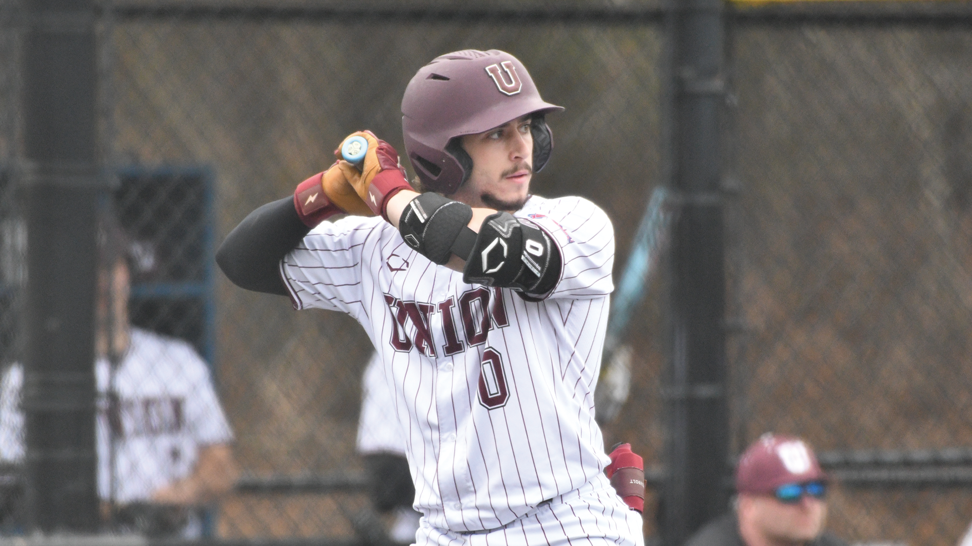 a baseball player wearing a white, pinstriped jersey and a garnet-colored helmet at bat with his bat resting on his shoulder