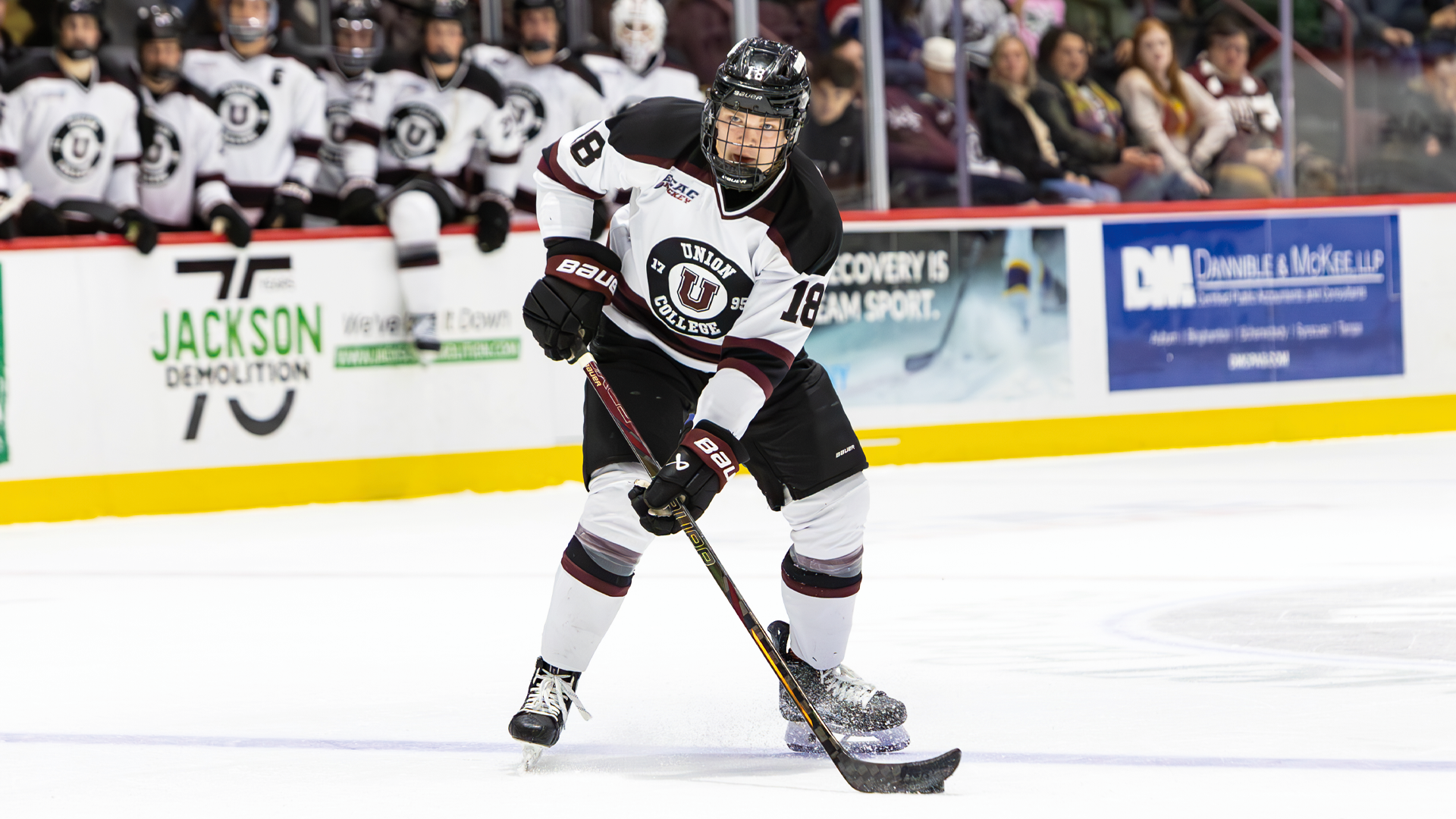 men's hockey player with the puck at this stick, standing on the ice looking up to make a pass