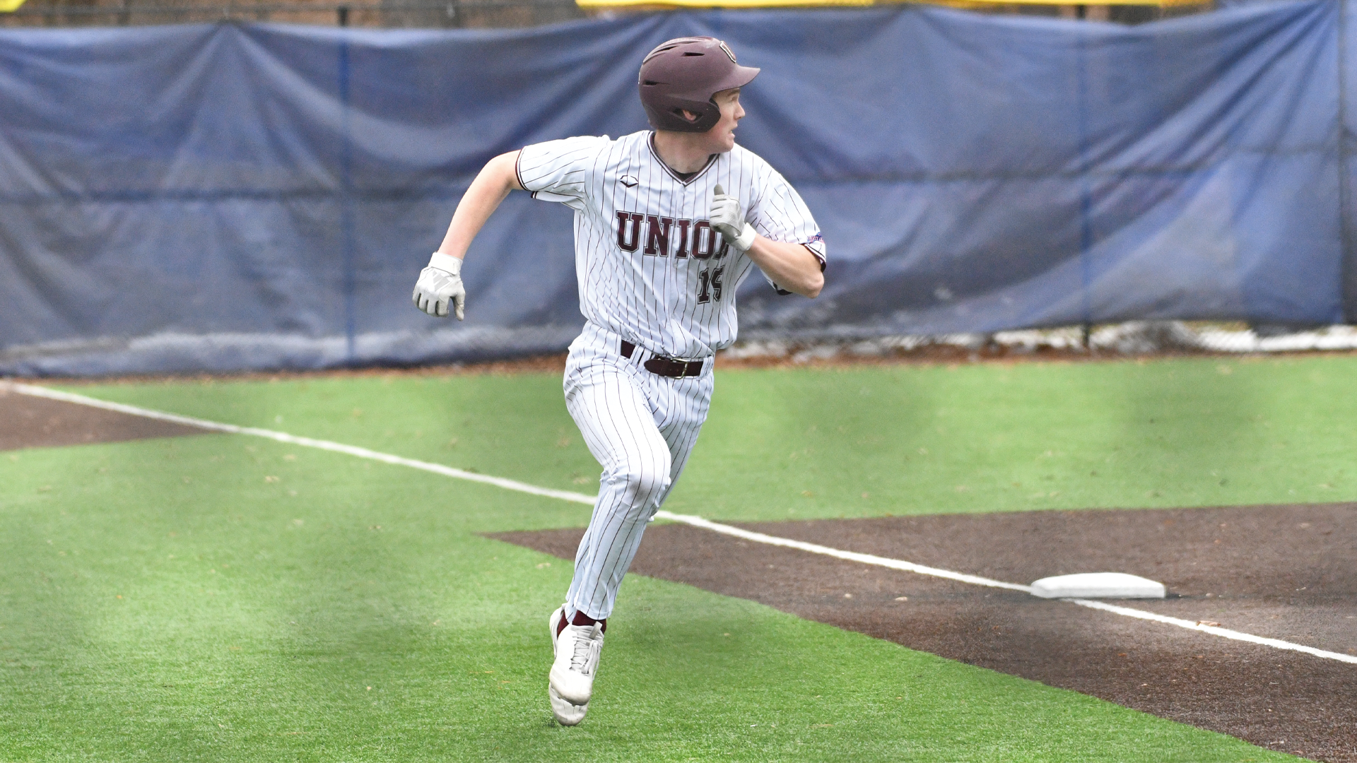 a baseball player looking over his shoulder as he rounds third base and heads towards home