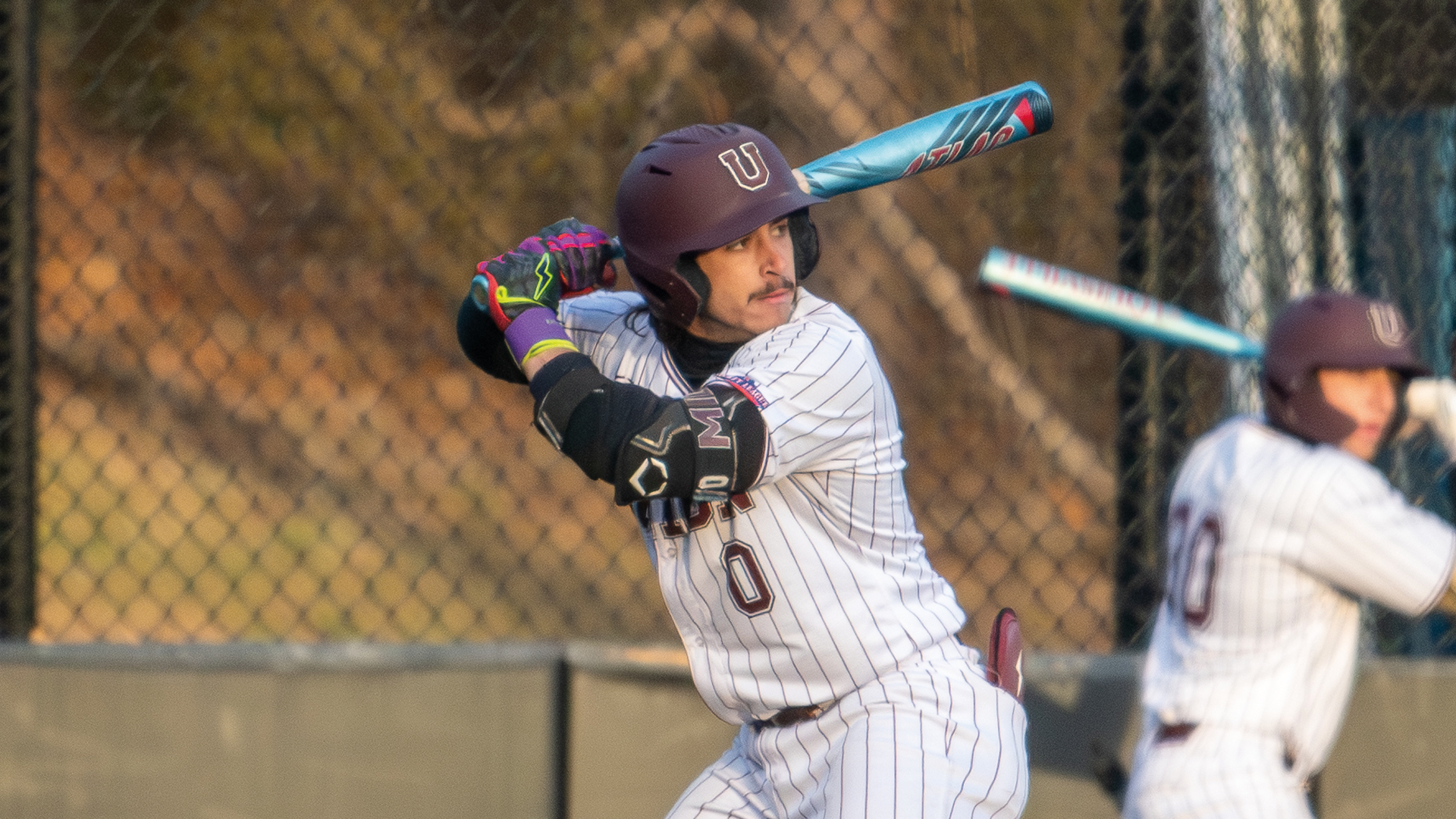 a baseball player wearing a white pinstriped jersey, photographed from the waist up while in his batting stance. The sun is setting in the photo, giving the picture an golden-orangish glow