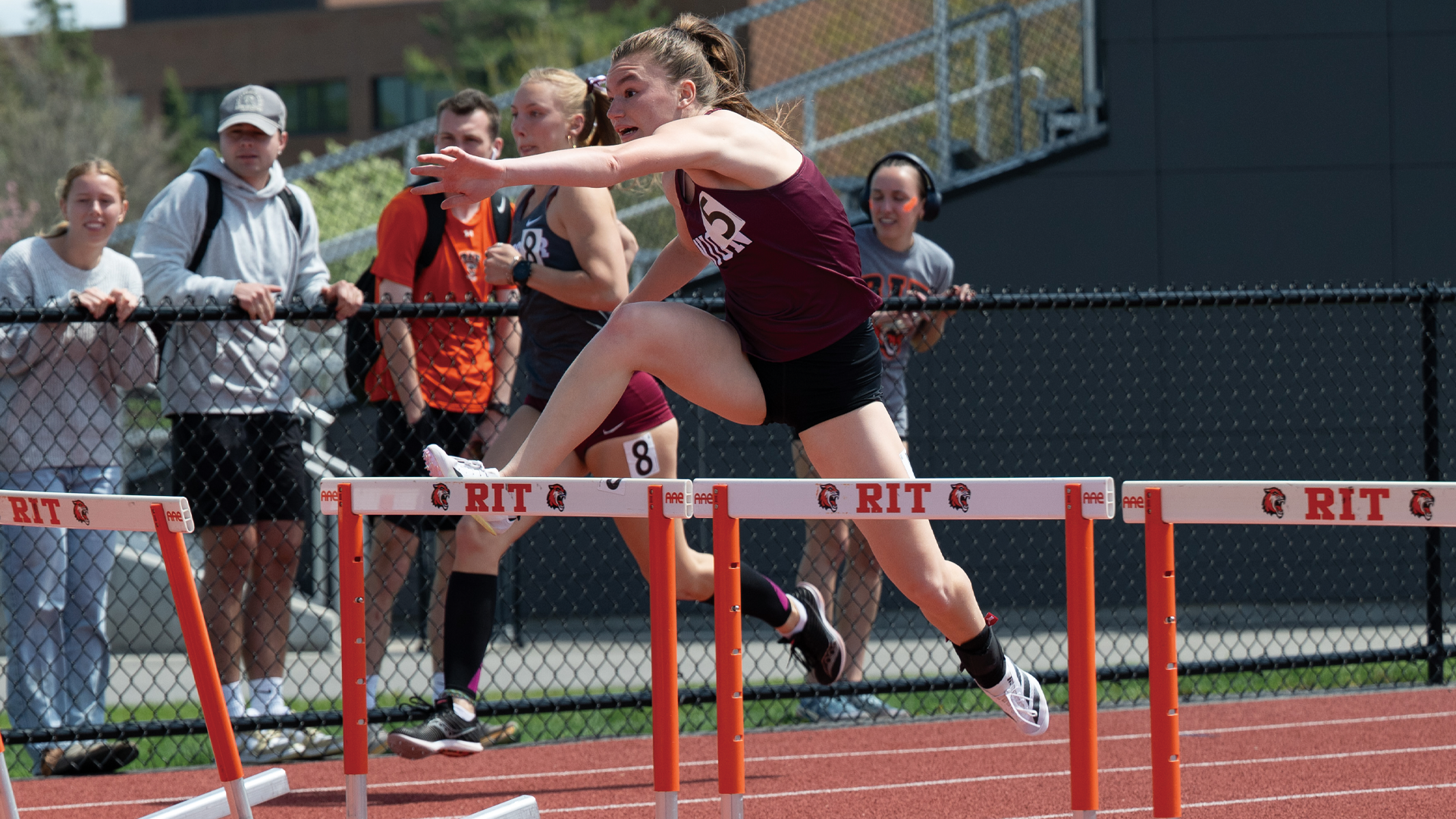 a women's track & field athlete leaping over a hurdle