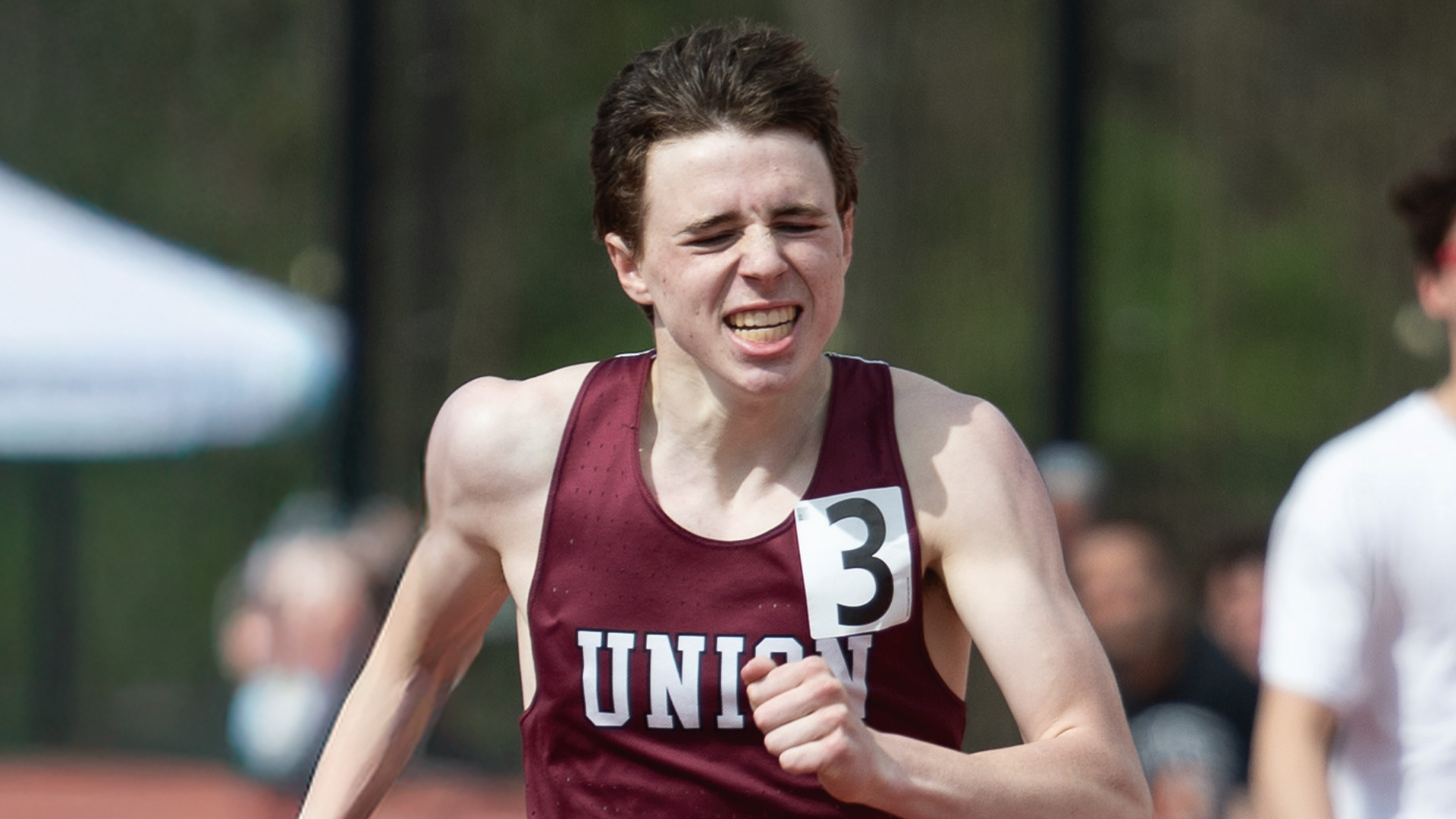 a men's track runner grimmacing as he runs