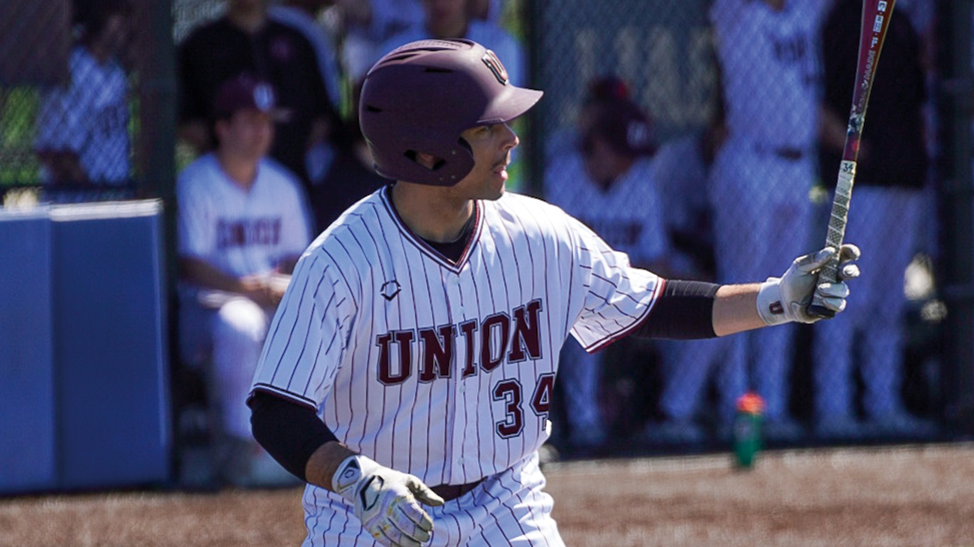 a waist-up photo of a baseball player in the batters box, facing the pitcher with his left arm outstretched and holding his bat