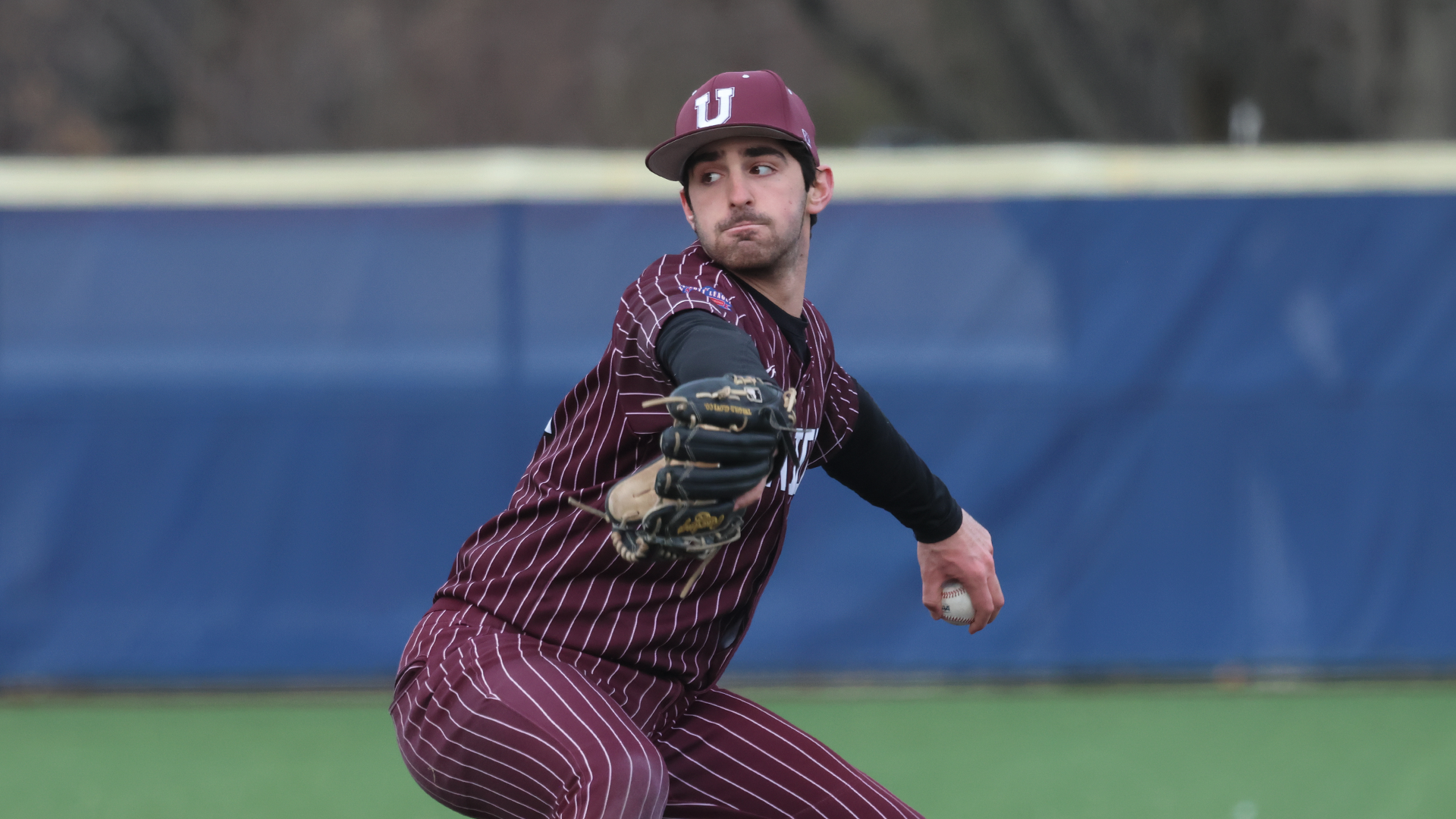 a right-handed pitcher pitching the ball, wearing an all-garnet uniform with white pinstripes.