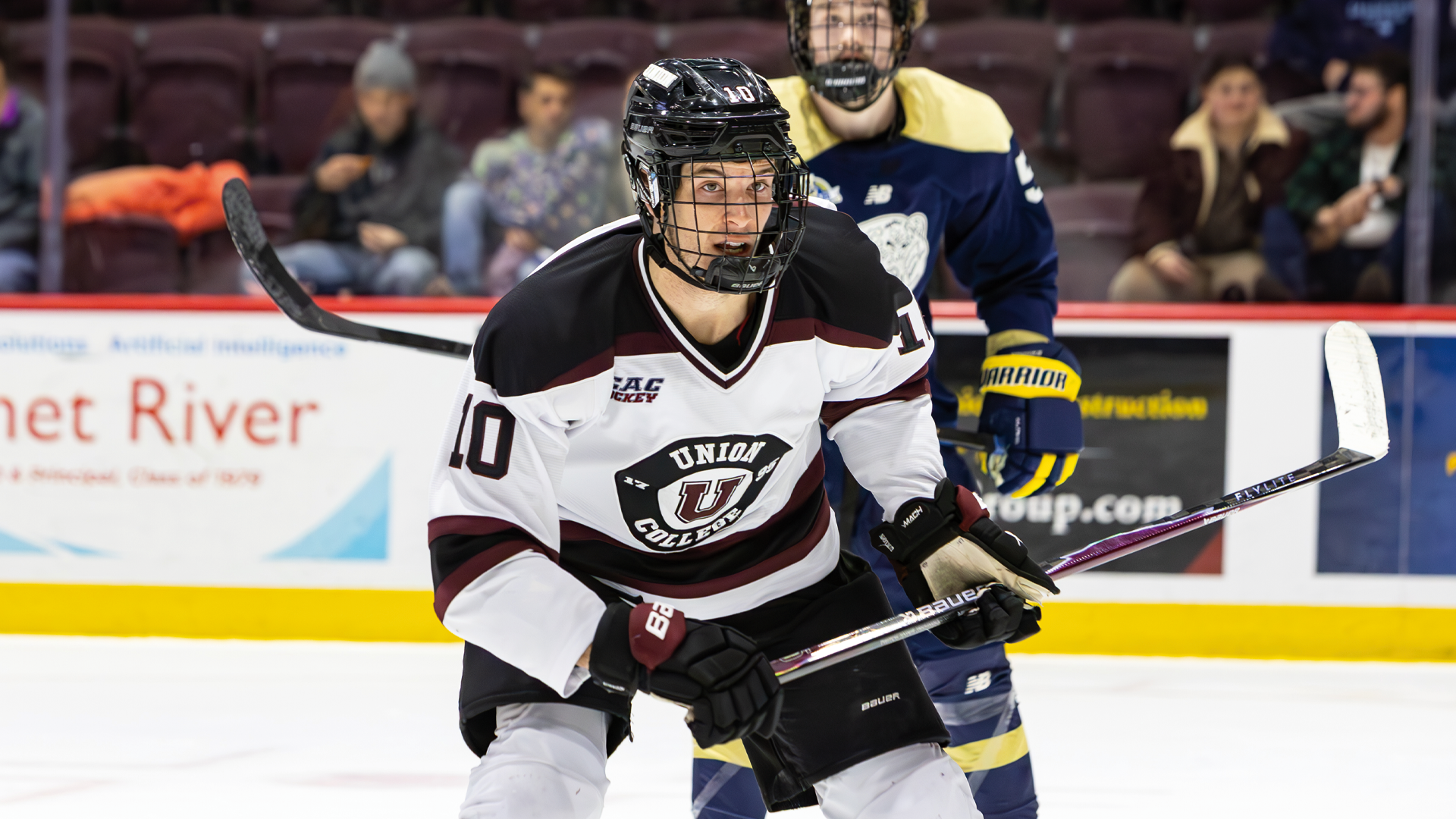 a men's hockey player wearing a black helmet and white jersey looking across the ice