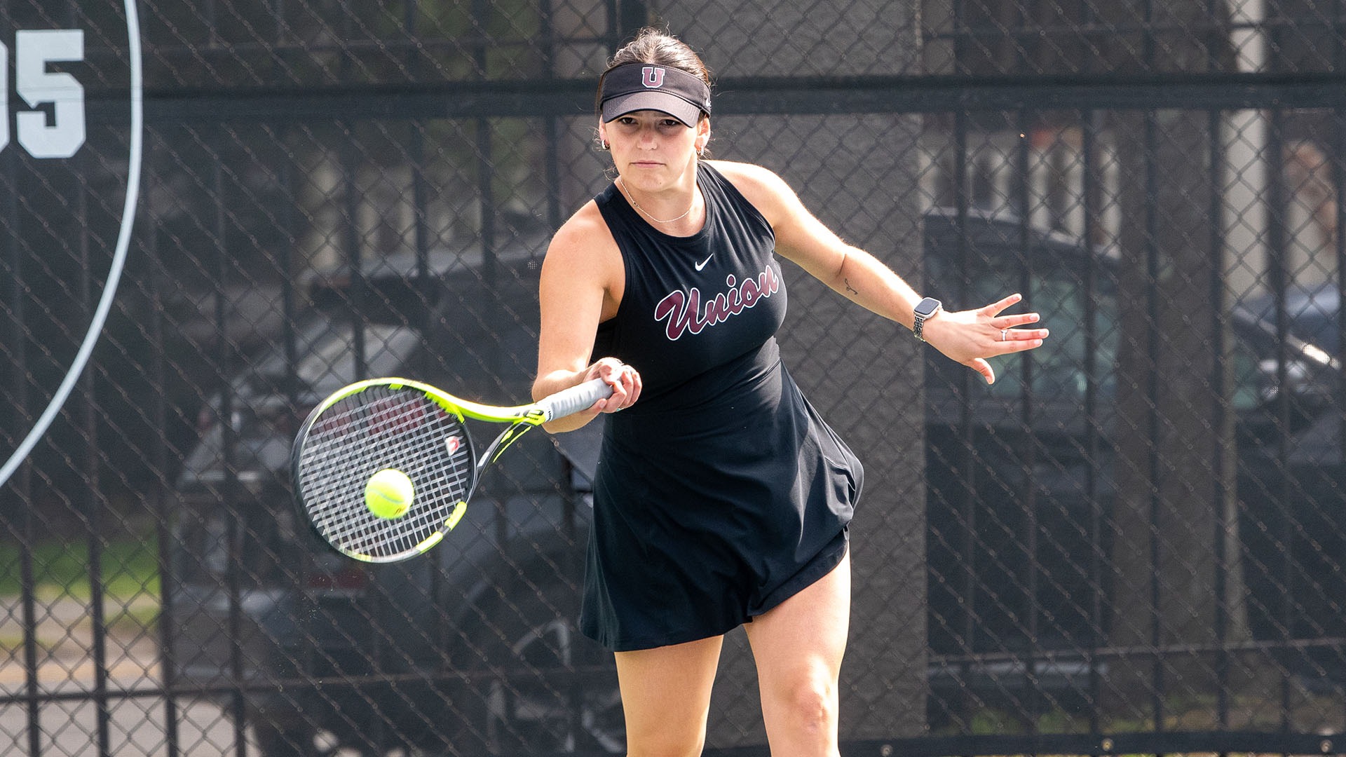 A tennis player wearing a black jersey hits a forehand.