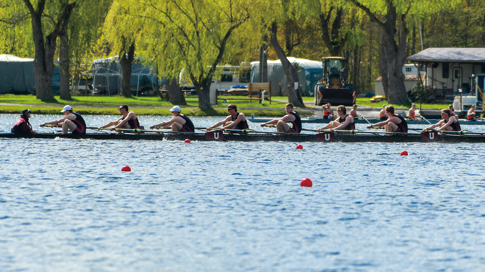 a men's crew team racing on blue water with bright green trees in the background