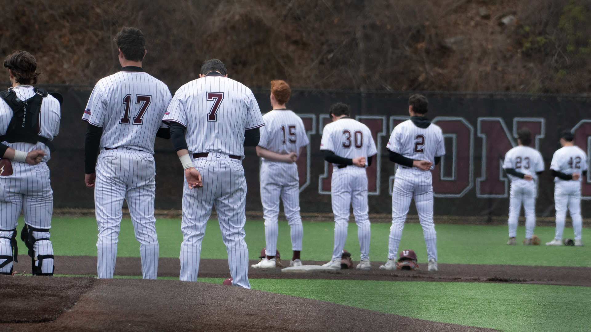the backs of baseball players as they stand in the field during the pregame anthem