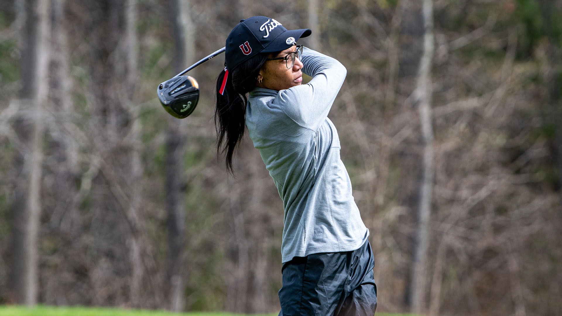 A golfer follows through with her swing on the tee box.