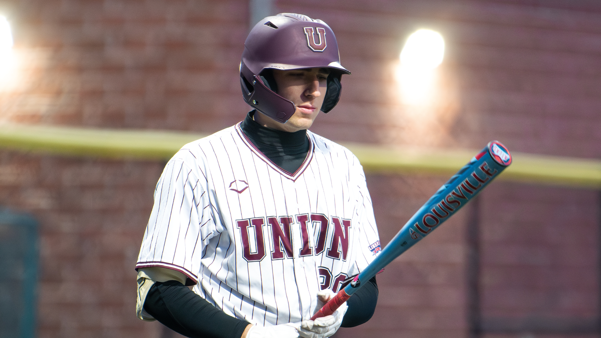 a baseball player looking down at his bat, wearing a white jersey with 
