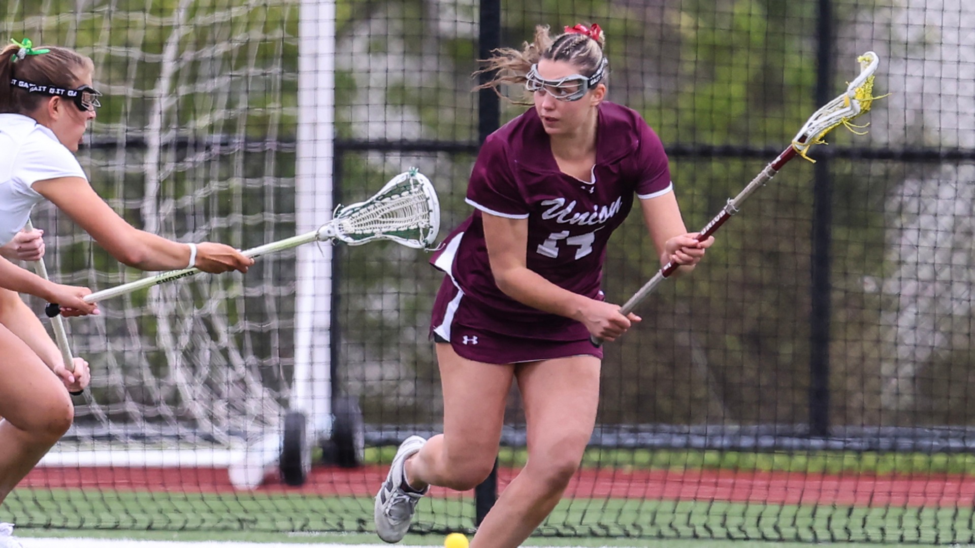 A Union lacrosse player holds the ball in her stick while dodging a defender.