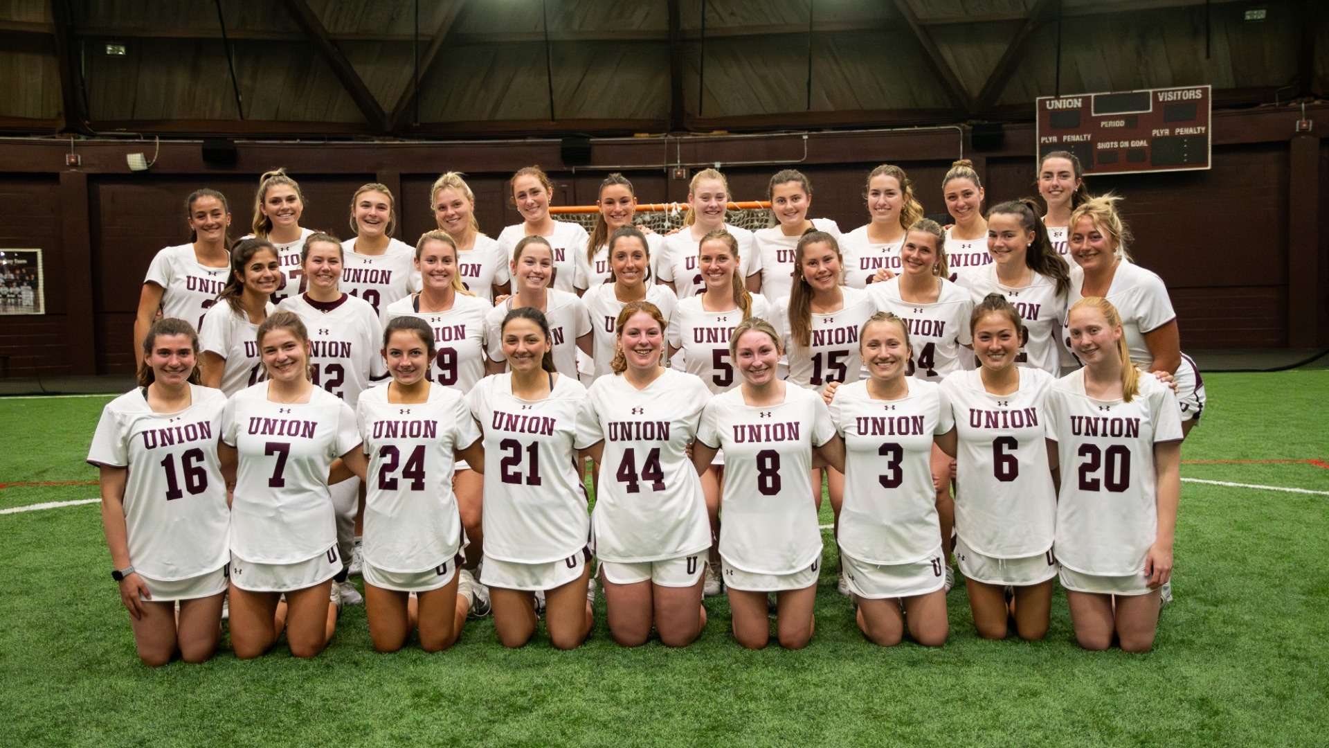 a women's lacrosse team wearing white jerseys, posed for a team photo