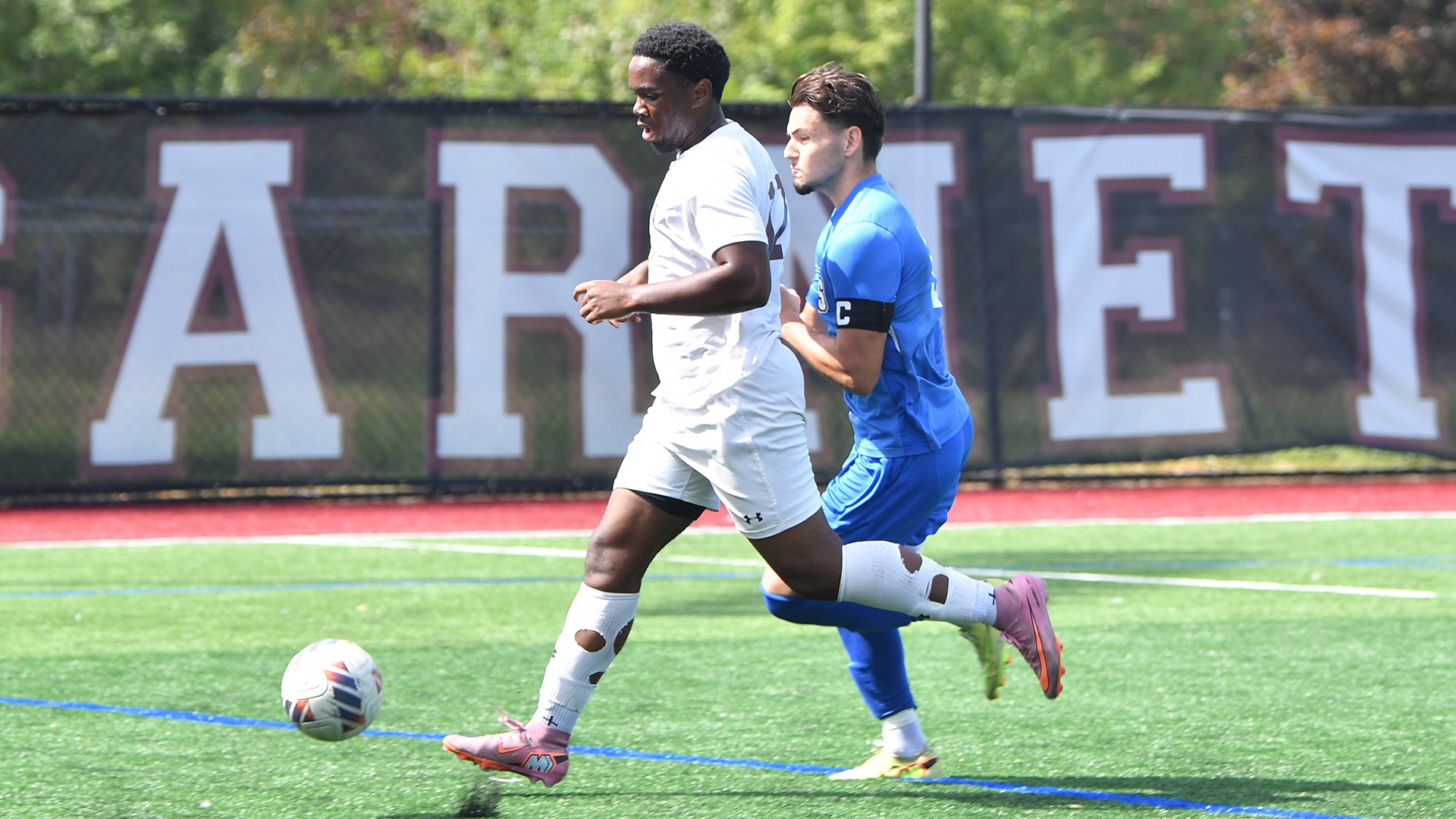 A soccer player chases after a ball with an opponent in pursuit