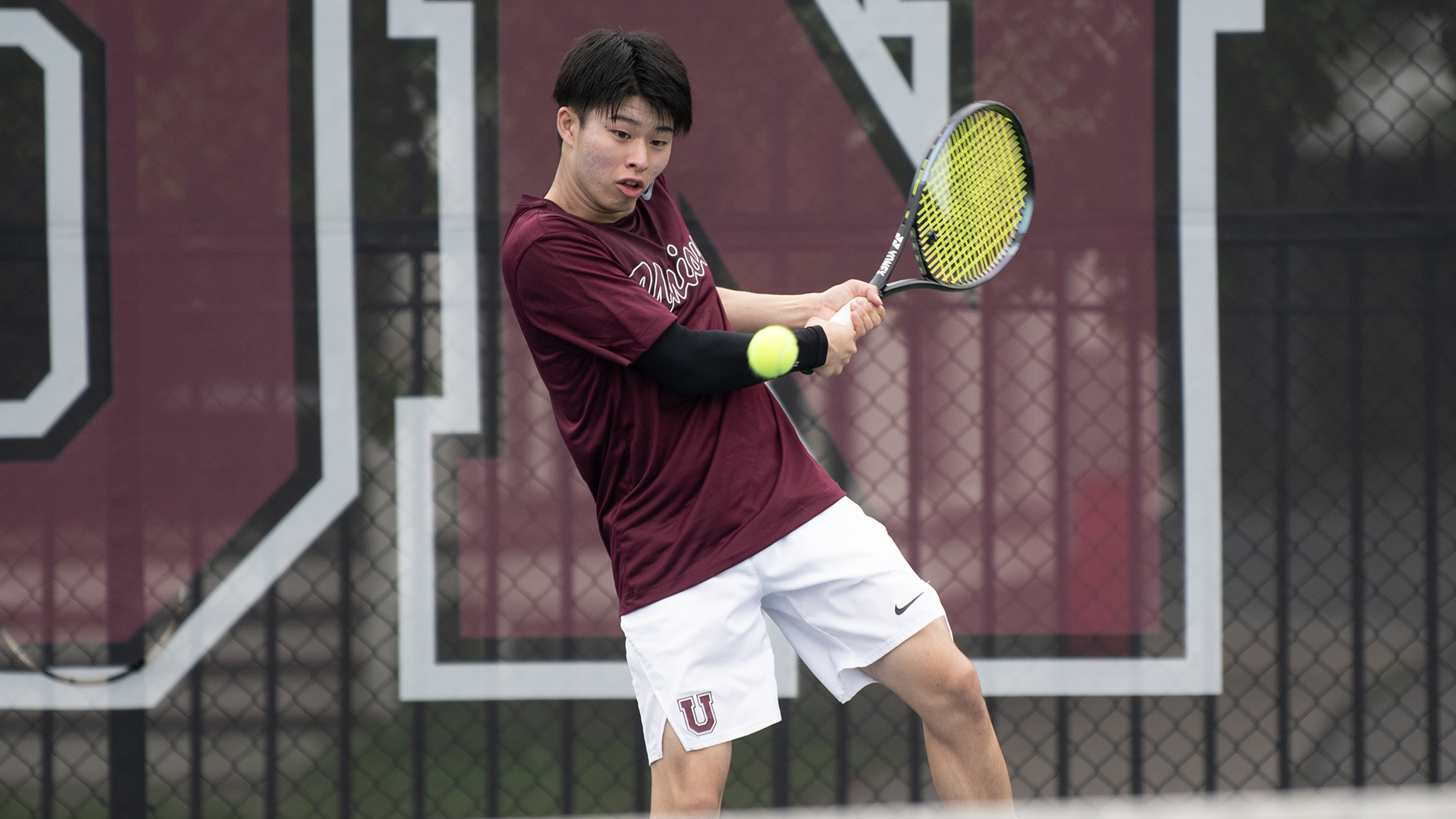 A Union tennis play prepares to hit a backhand with the ball right in front of him.