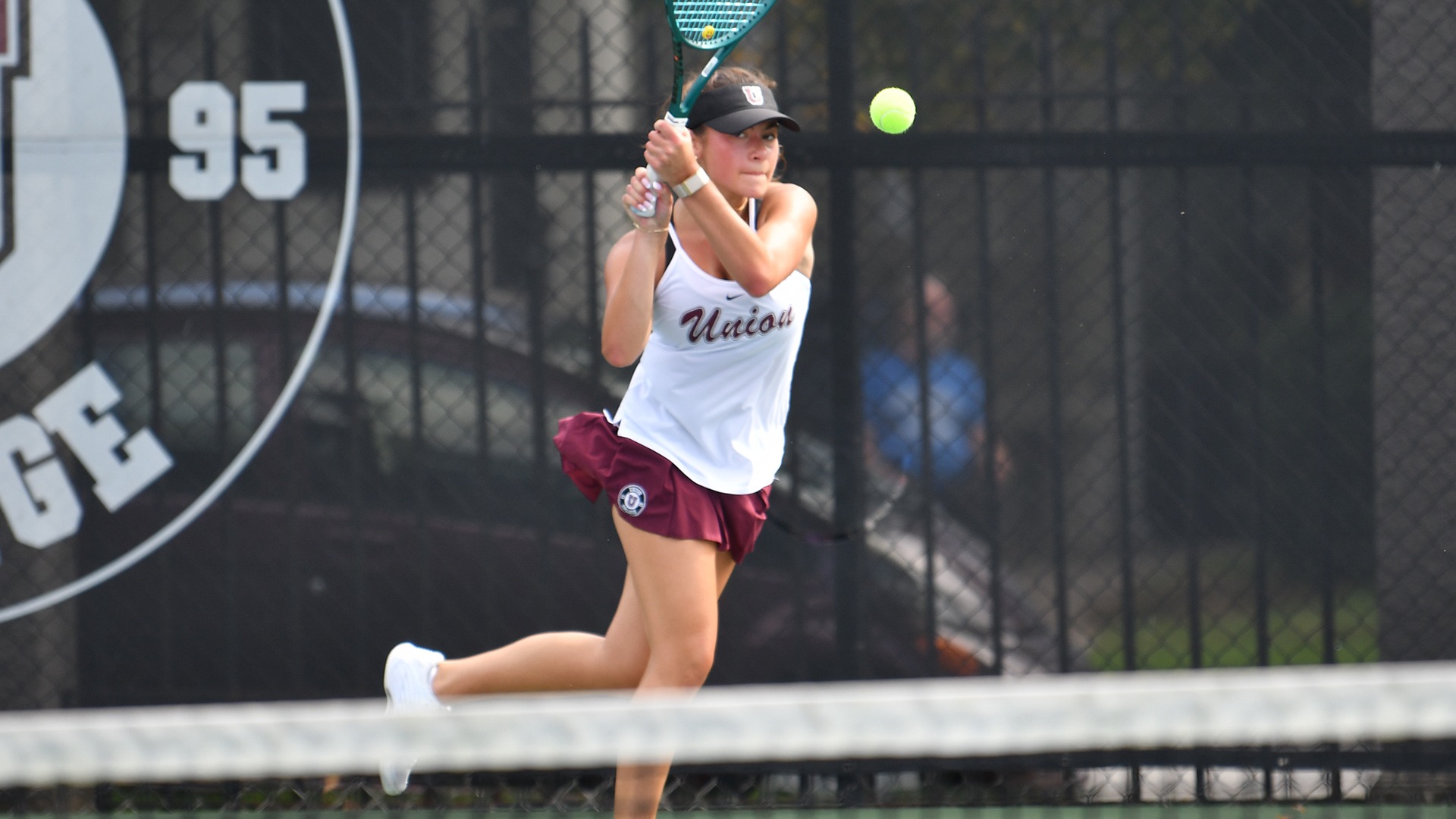 A Union women's tennis player watches the ball after following through on a backhand.