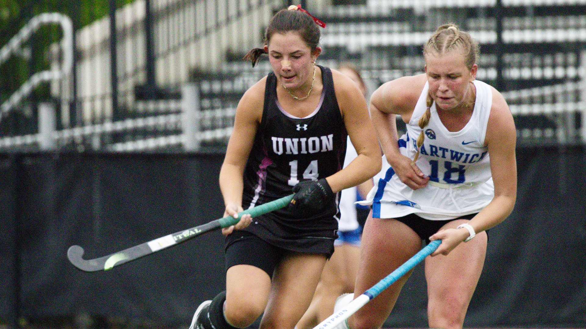 A Union field hockey player stickhandles the ball with an opponent trailing behind.