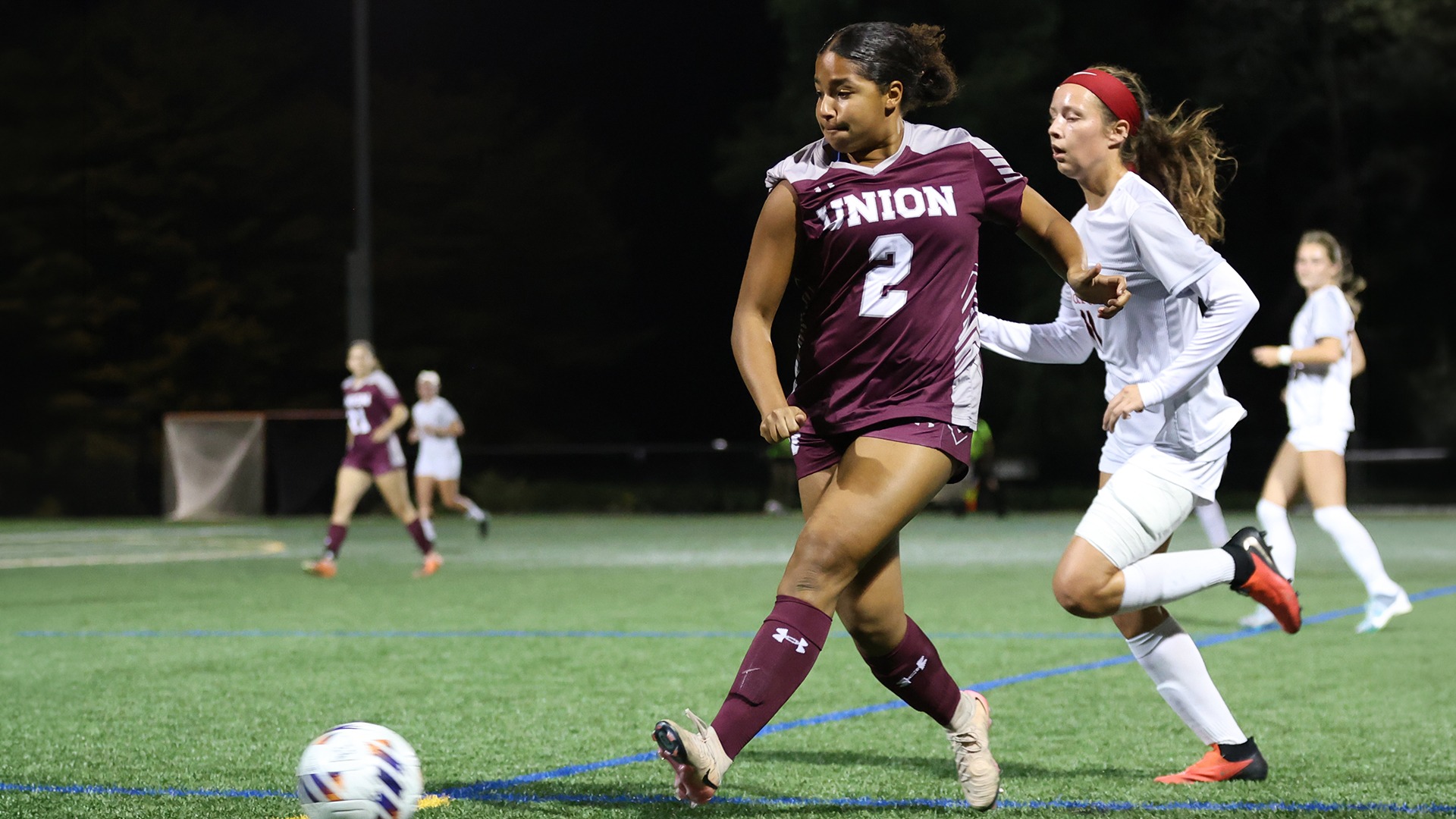 A soccer player kicking a ball under the lights.