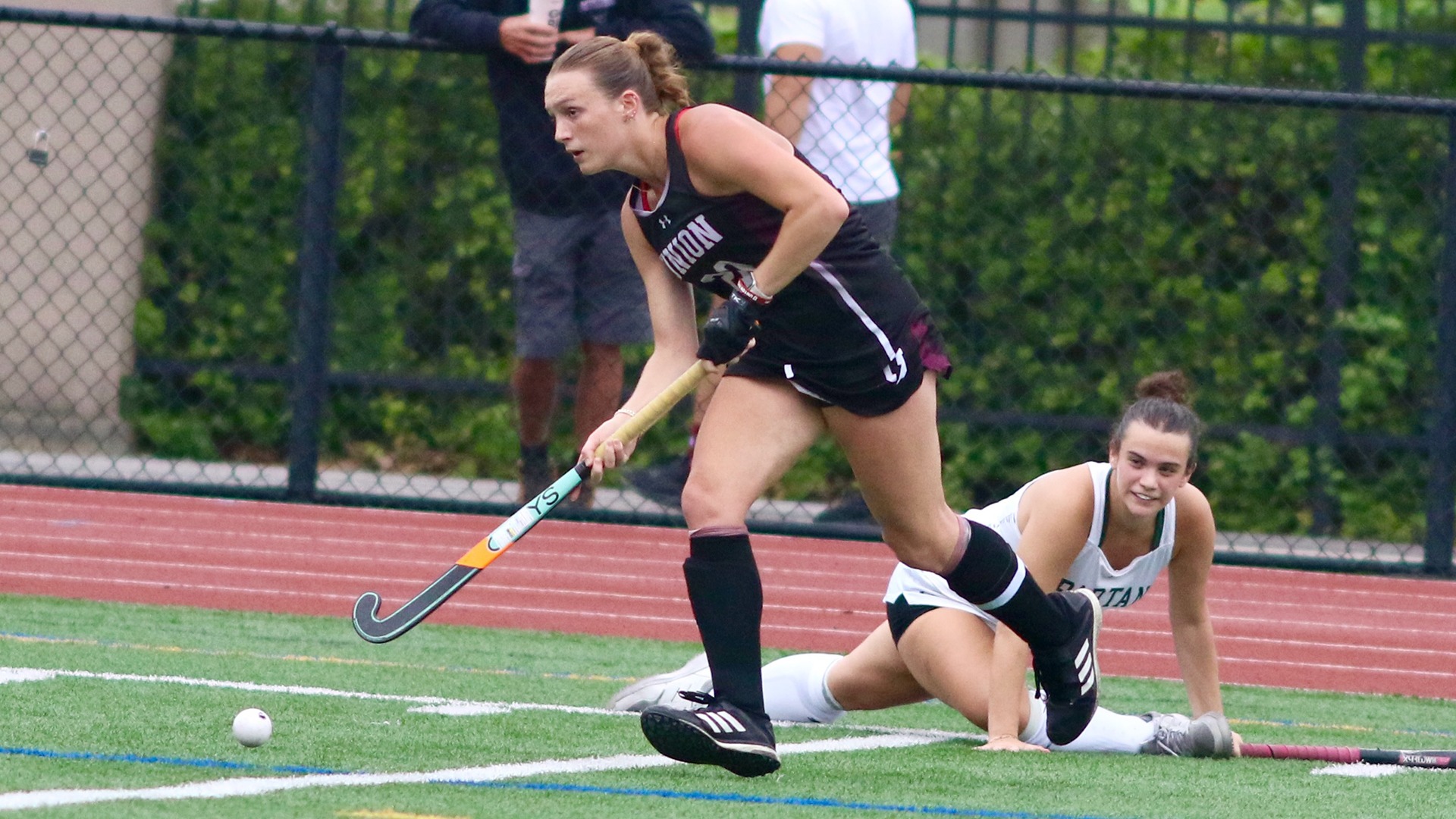 A Union field hockey player looks for a pass with an opponent on the ground behind her.