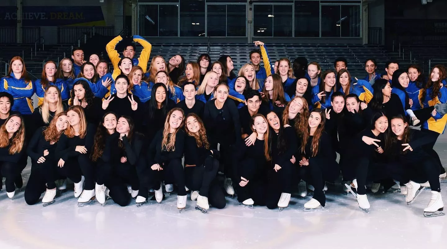 The UD Figure Skating team poses on the ice in matching blue and black jackets.