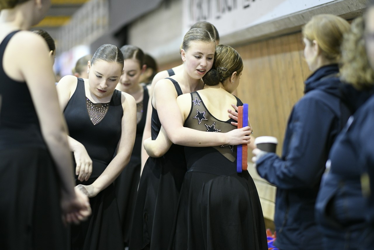 Two synchronized skaters embrace backstage after a competition
