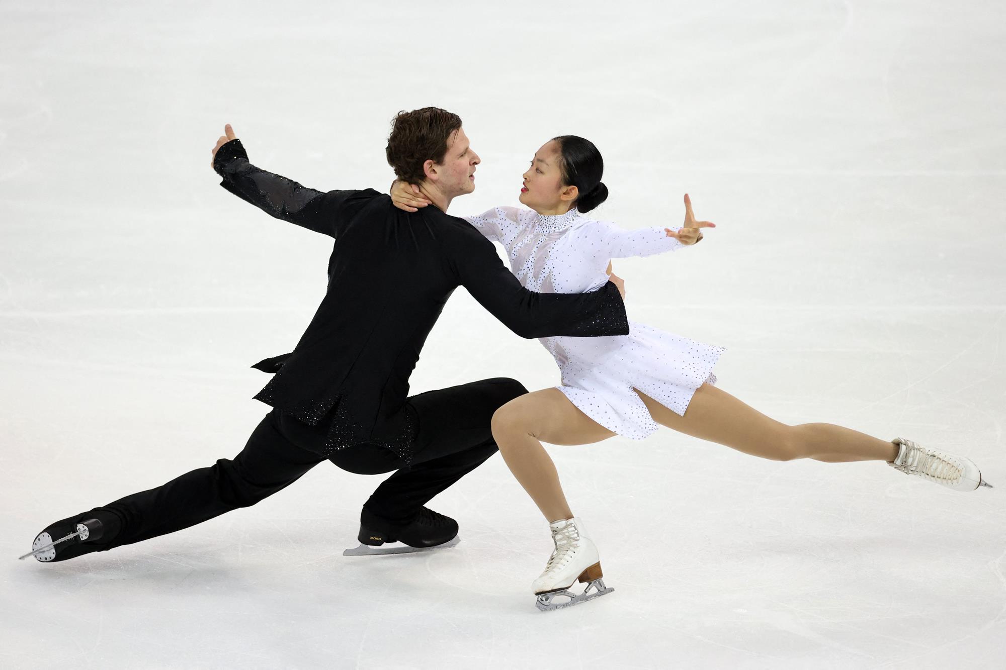 Misha Mitrofanov and Audrey Lu perform a spin low to the ice with their right arms outstretched. 