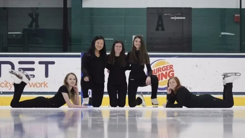 Several skaters in all black pose on the ice, some laying down.