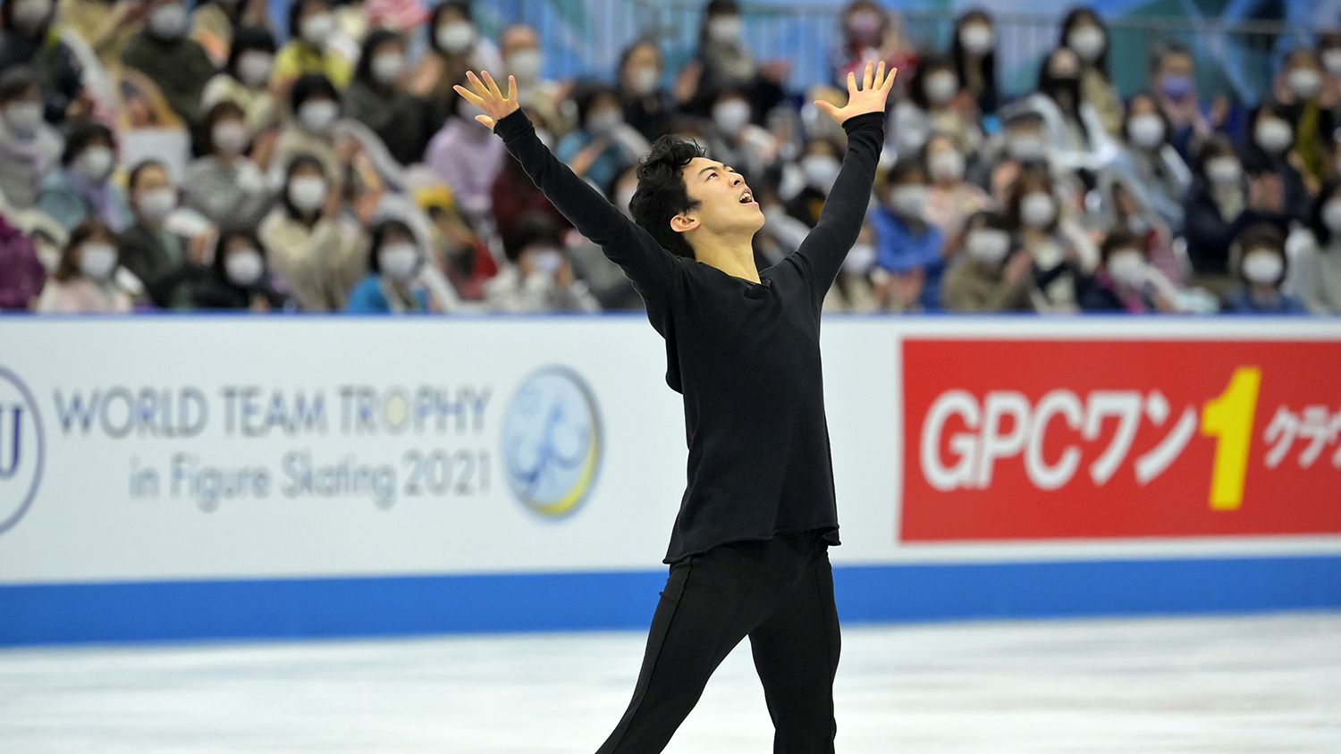 Nathan Chen, wearing all black, stands at center ice with his hands stretched towards the sky as he concludes his free skate.