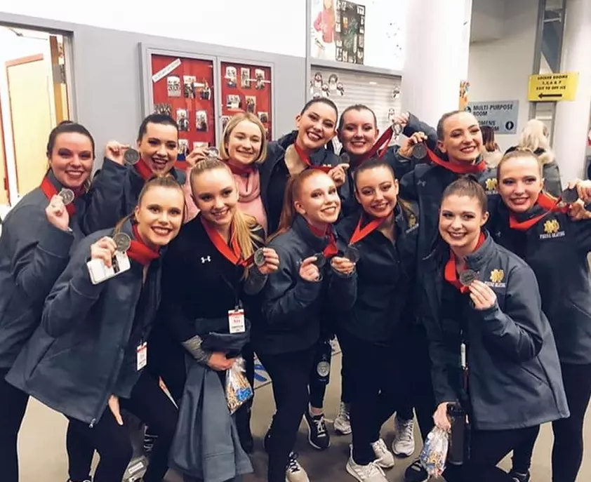 Skating team posing in their jackets and holding up medals