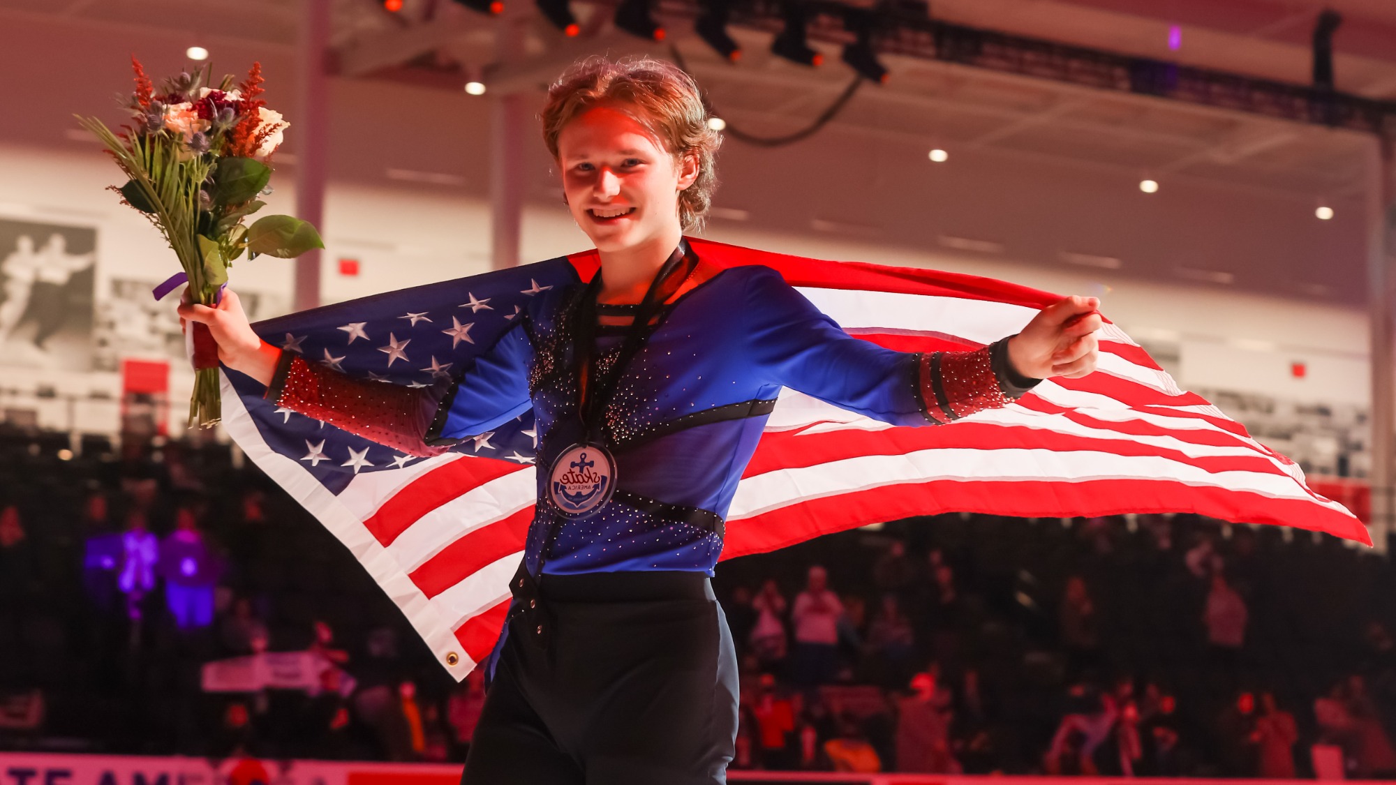 Ilia Malinin poses with the American flag, wearing his gold medal, after winning Skate America.