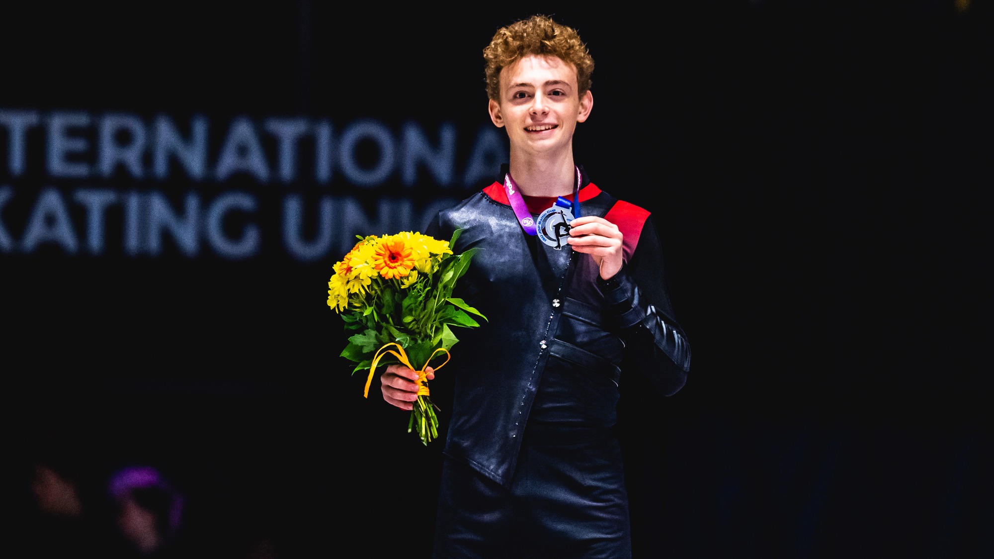 Robert Yampolsky smiles as he stands on the podium and holds up his silver medal at JGP Poland 2.