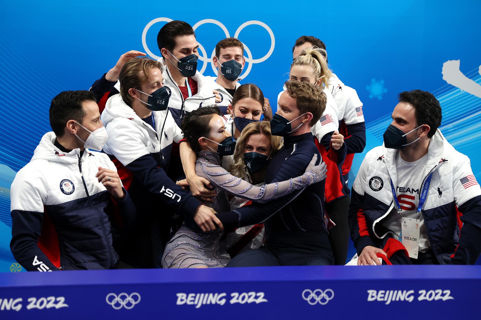 Madison Chock, Zachary Donohue, Kaitlin Hawayek, Jean-Luc Baker, Brandon Frazier, Ashley Cain-Gribble and Timothy LeDuc embrace Madison Chock and Evan Bates in the kiss and cry after winning the team event free dance in Beijing